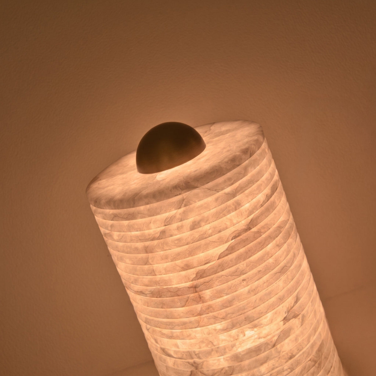Aurelior Small LED table lamp with ribbed alabaster cylindrical body glowing warm white, topped with a rounded brass cap, shown close-up against a plain background.