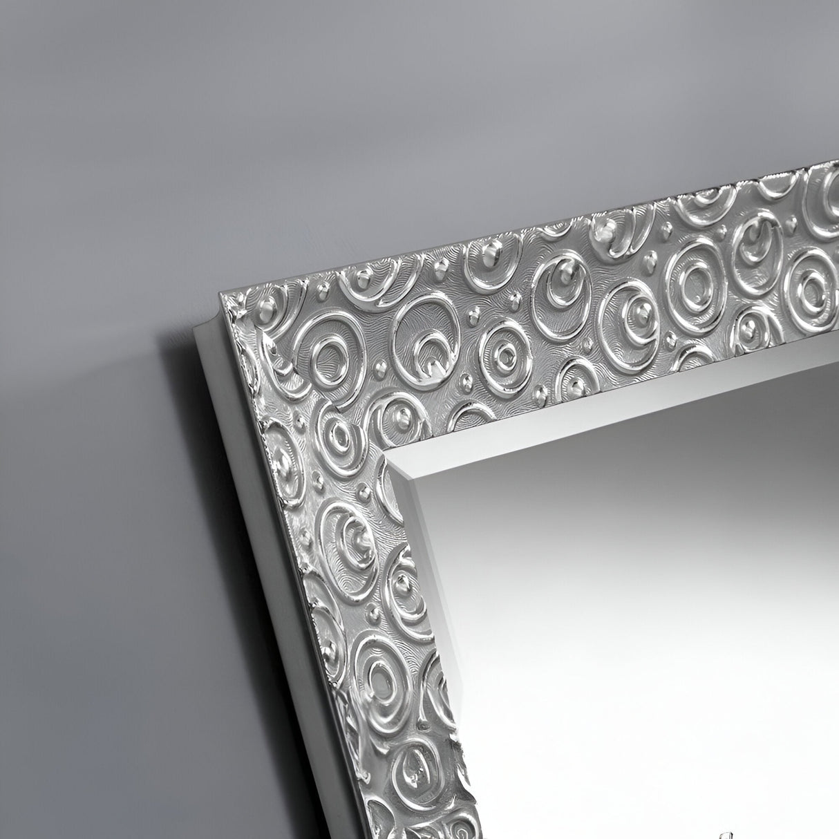 A closer look at the Astral Rectangle Wall Mirror - Silver unveils its intricate silver wood frame. Featuring a circular embossed pattern, it presents a textured, reflective surface set against a sleek gray background.