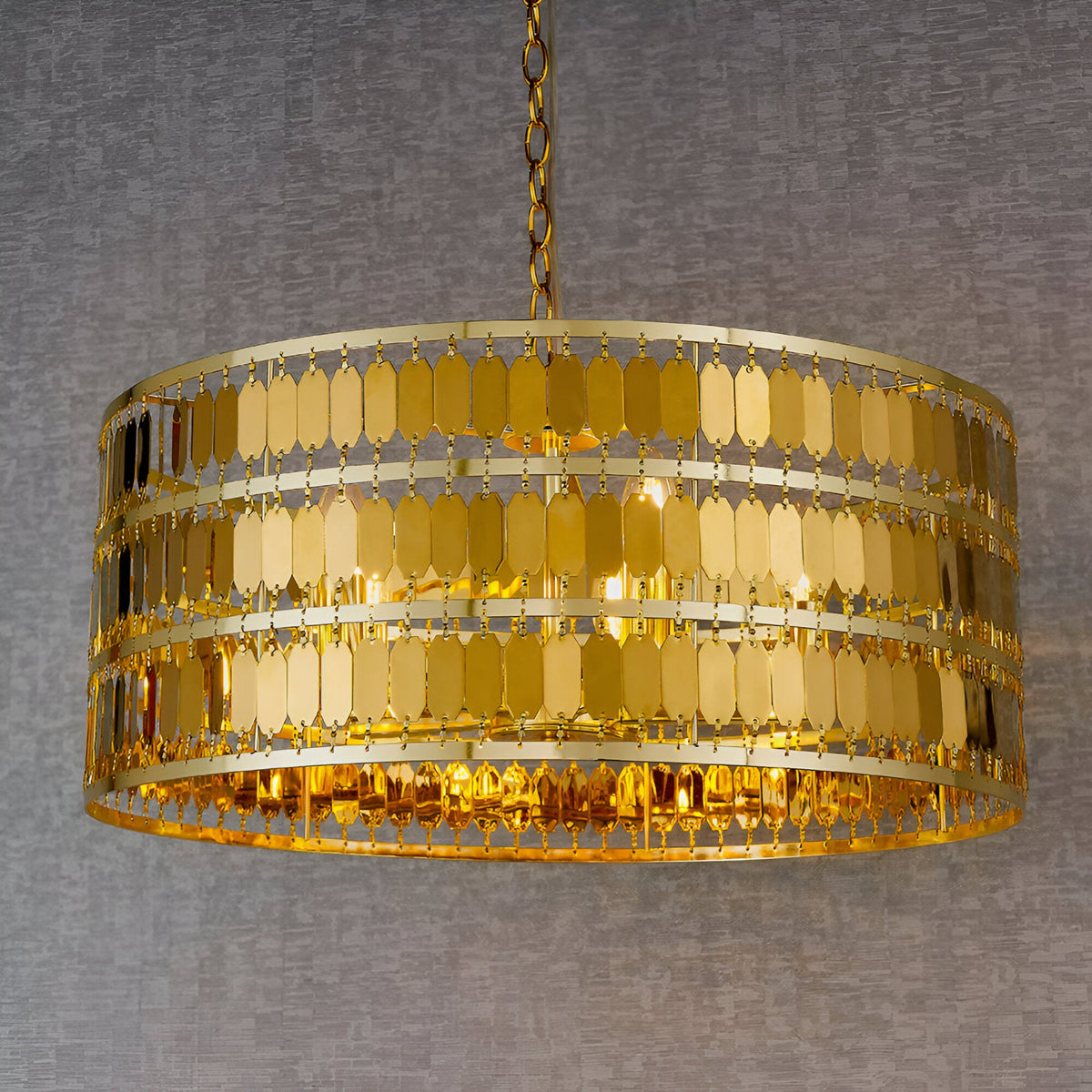 Brackhurst 5 Light Pendant in gold, drum-shaped frame with tiered hexagonal metal plates catching the light, hung from a chain against a grey background.