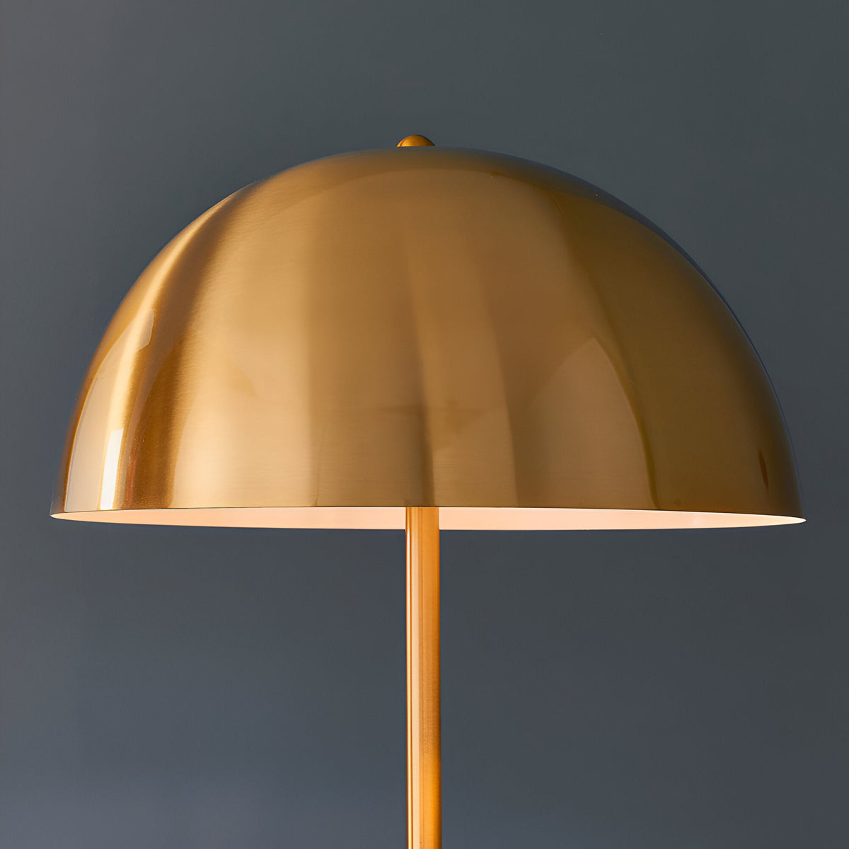 Endon Castford floor lamp close-up showing the antique brass dome shade with gloss white inner and slim brass stem against a dark grey background.
