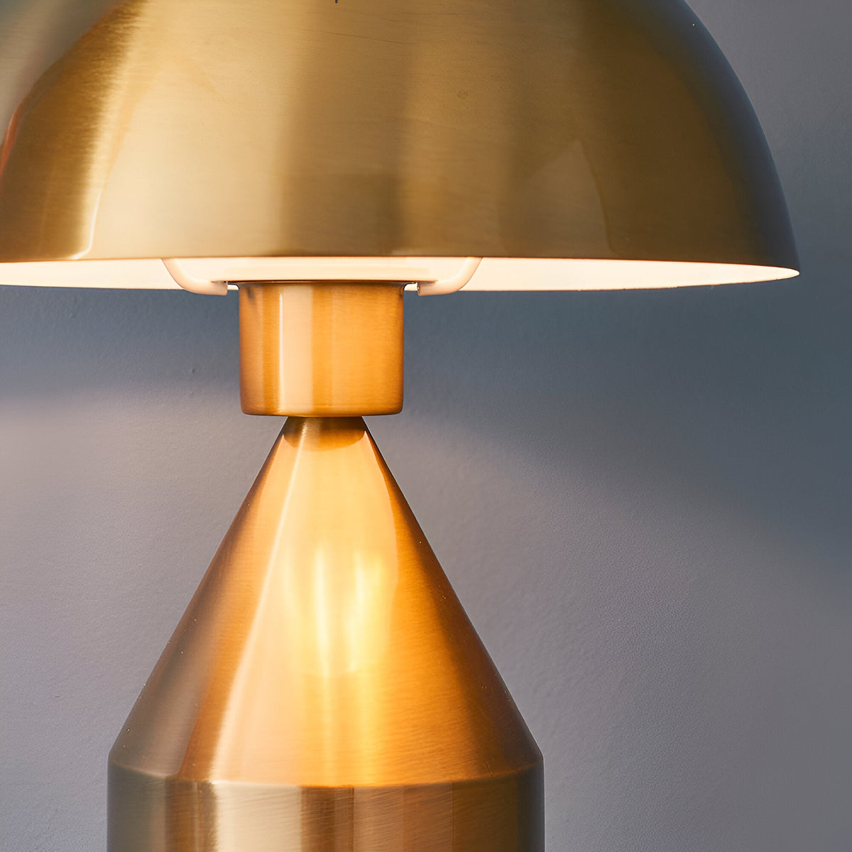 Close-up of the Castford Table Lamp in antique brass, showing the domed metal shade with white gloss interior above a tapered conical base.