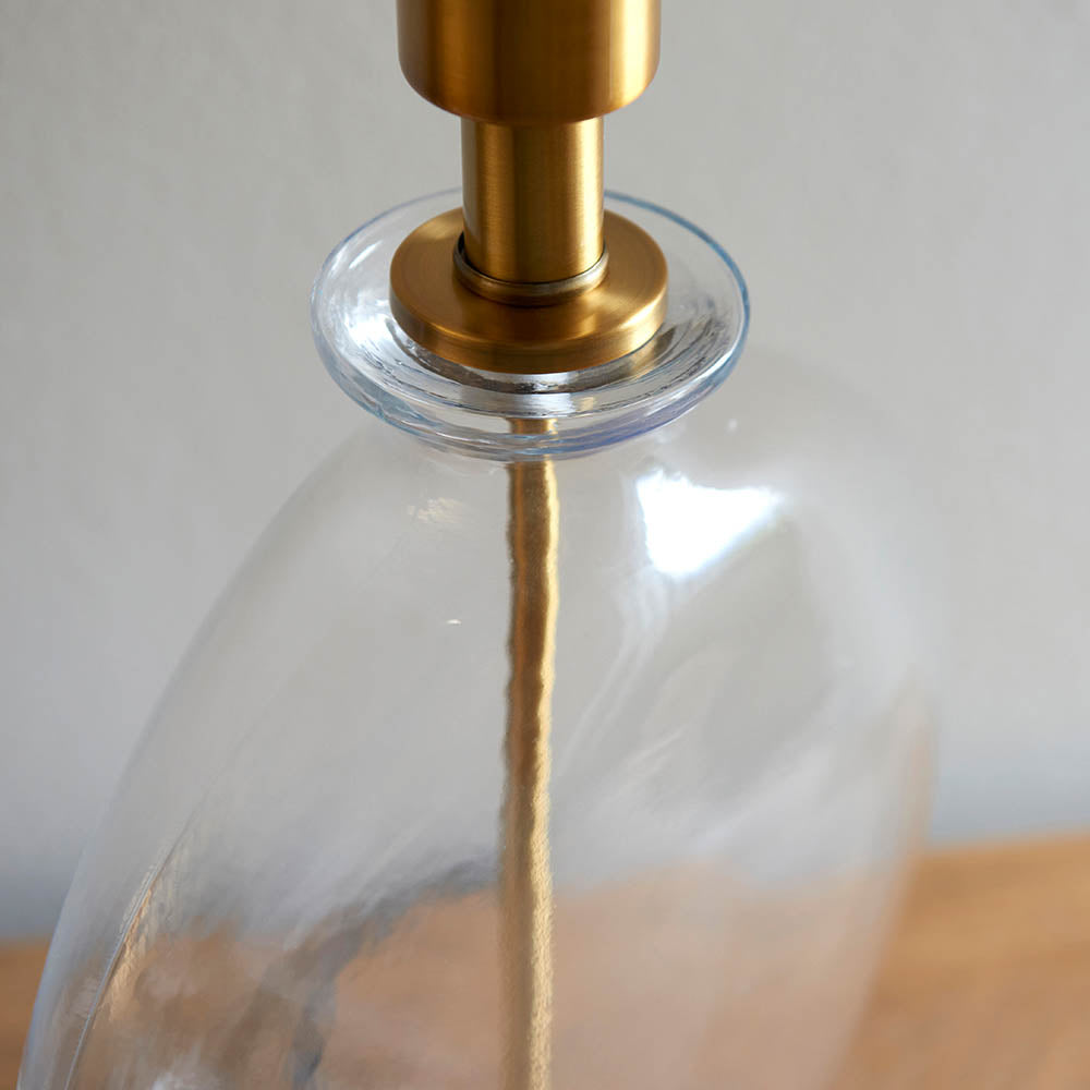 Close-up of the Endon Bramleigh table lamp showing the clear glass ellipsoid base and antique brass neck fitting.