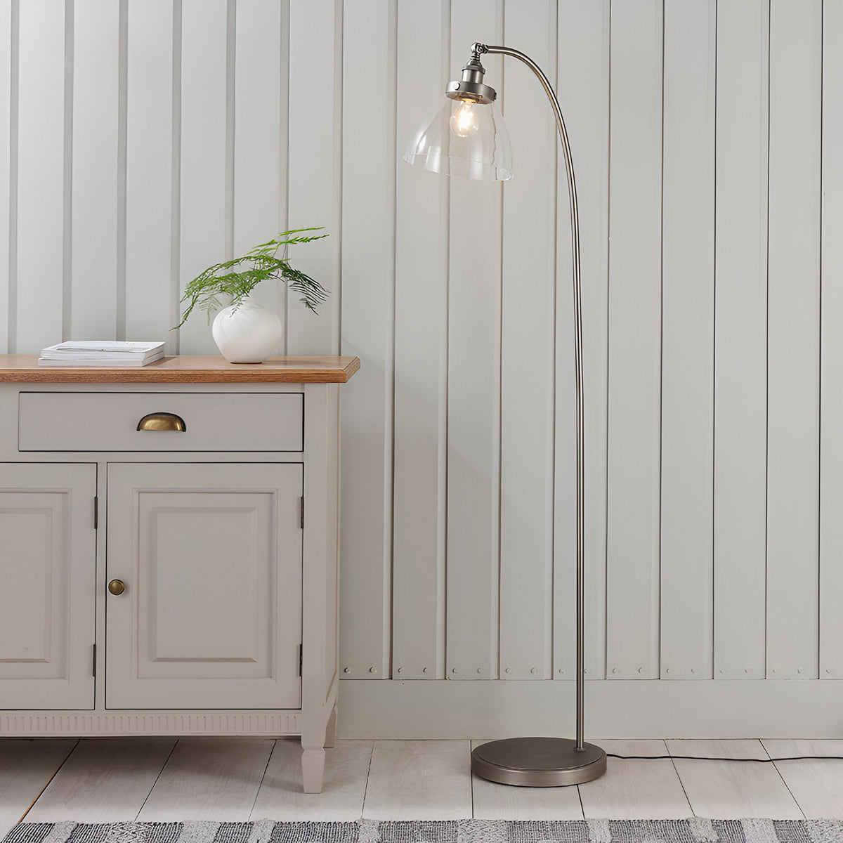 Endon Wentworth arc floor lamp in brushed silver with clear glass shade and E27 filament bulb, beside a grey sideboard in a panelled living room.