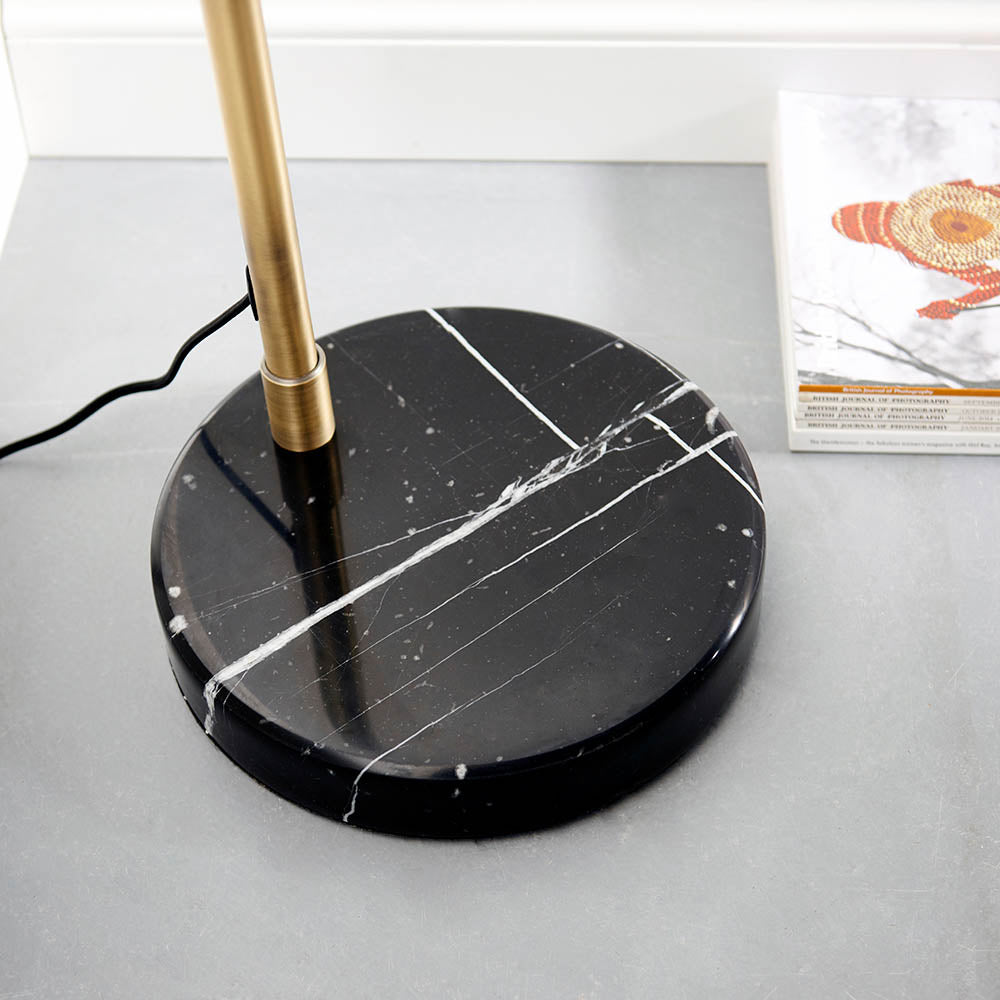 Sinclair Floor Lamp base close-up showing black marble with white veining and a brass stem, set on a grey surface near a magazine.