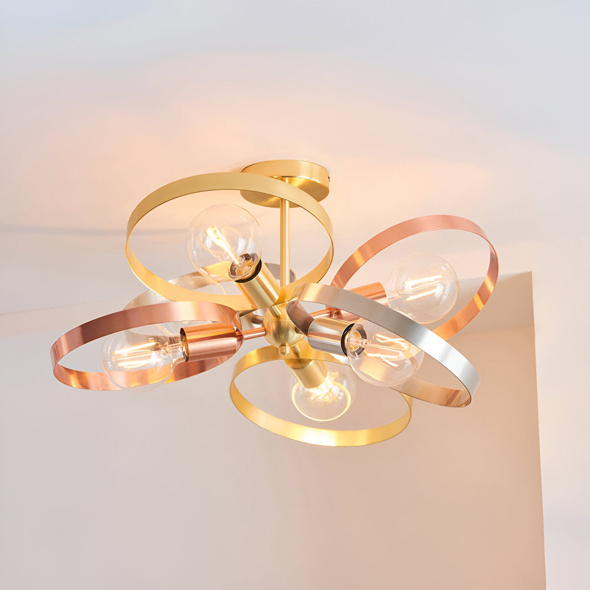 Endon Brenmere 6 light semi-flush pendant with open hoops in brushed brass, copper and nickel, exposed E27 bulbs, mounted to a white ceiling.