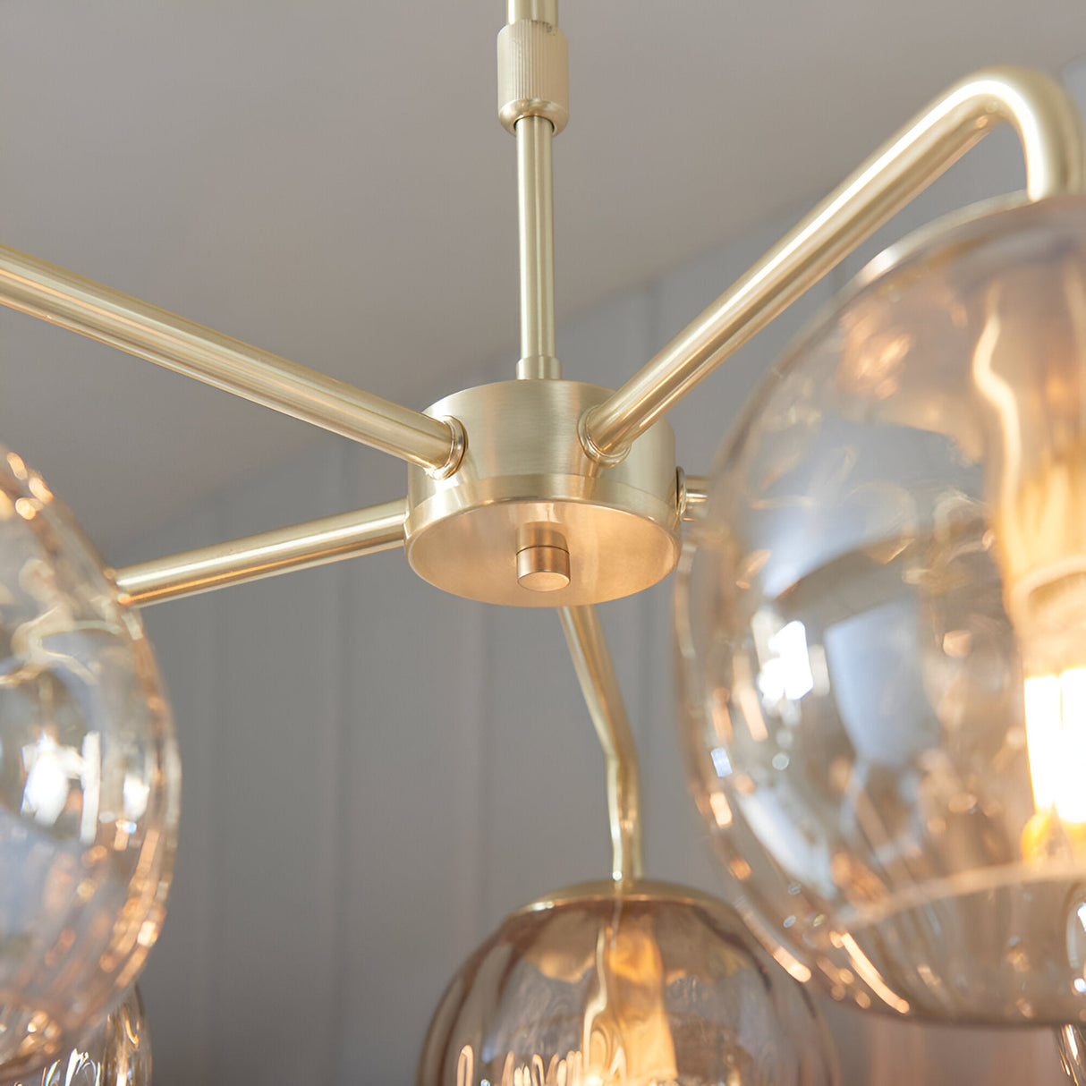 Close-up of the Endon Draycott 5 light pendant showing the satin brass ceiling plate, radiating arms and champagne dimpled glass shades.