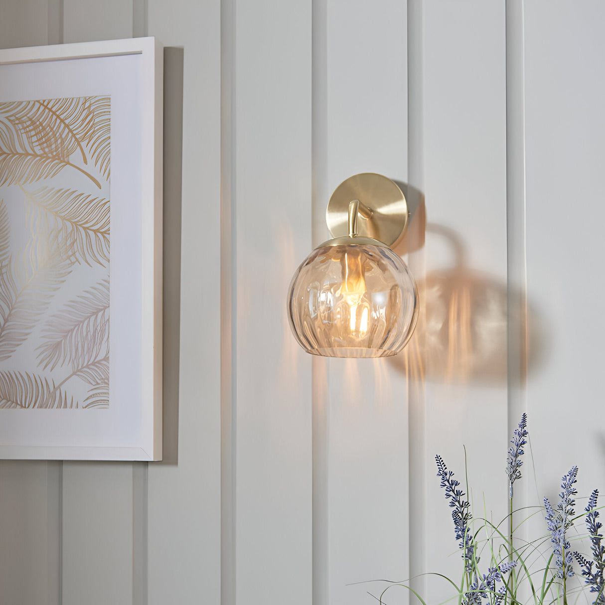 Endon Draycott wall light with champagne dimpled glass globe shade on satin brass arm, mounted on panelled wall beside framed botanical print.
