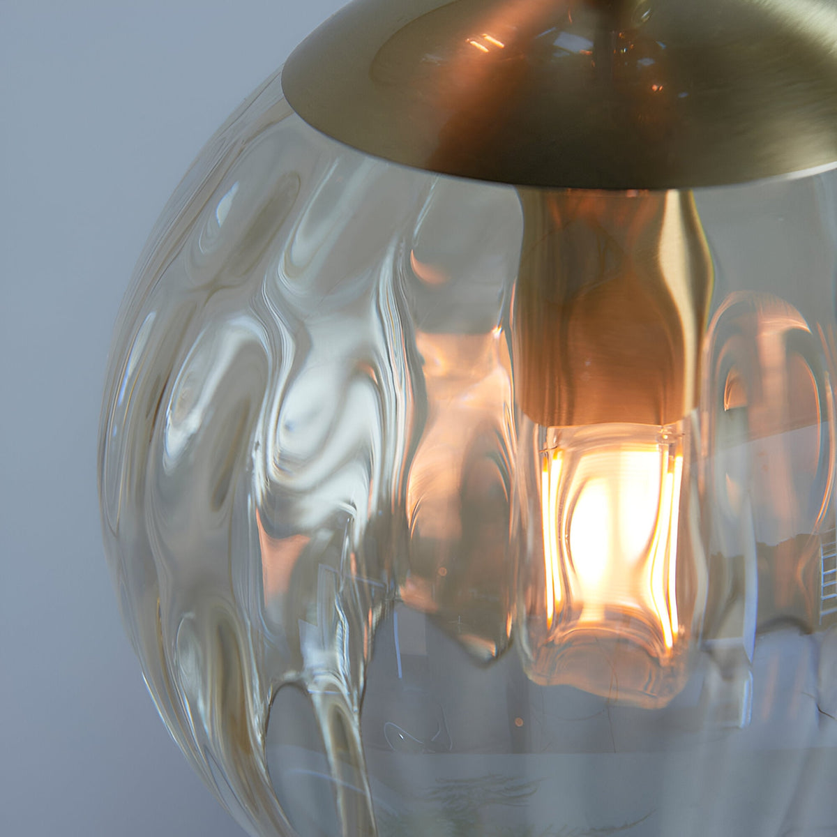 Close-up of the Draycott 3 Light Dimpled Glass Pendant in Satin Brass, showing a textured glass shade with a lit bulb beneath the brushed brass canopy.