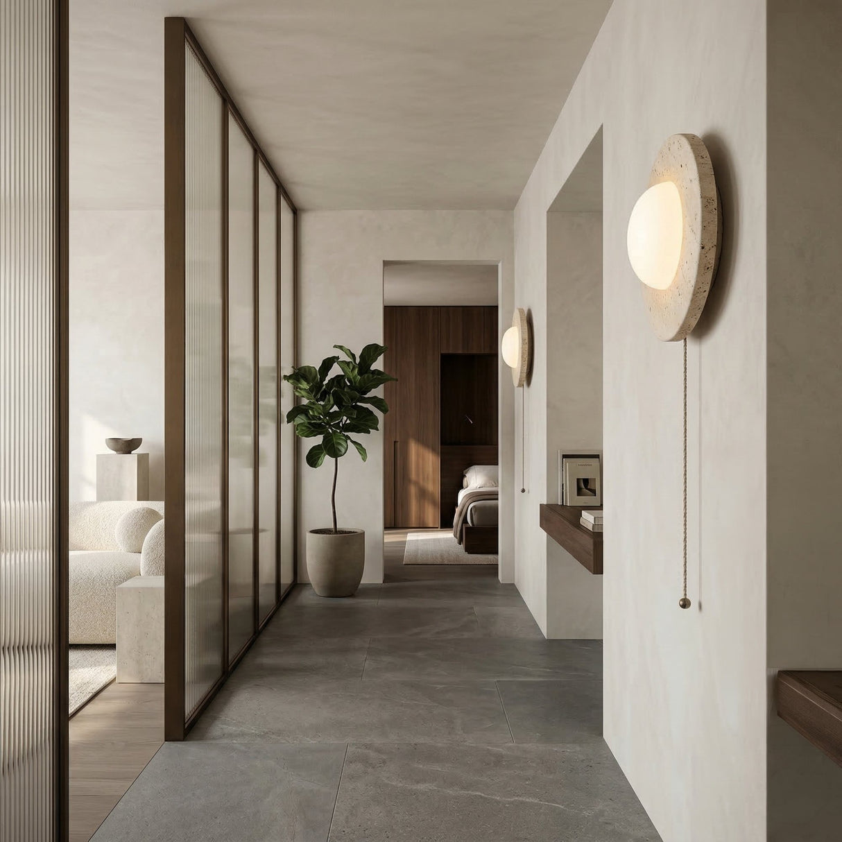 A modern minimalist hallway features light gray walls, large floor tiles, a potted plant, the Solenne 1 Light Travertine Wall Light With Pull Switch in light beige, and glass-paneled partitions separating it from the living area and bedroom.