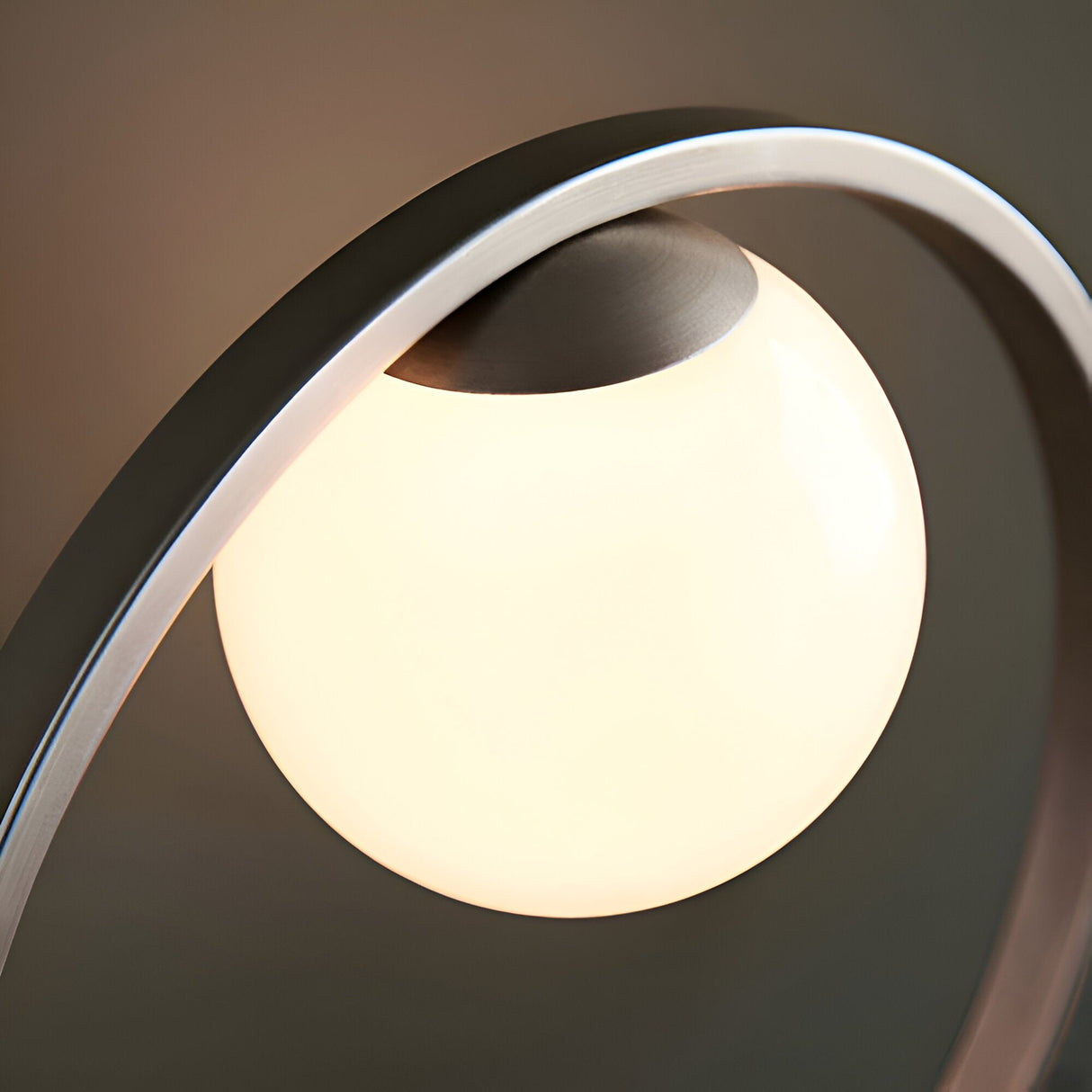 Brackstead Table Lamp in brushed silver, close-up of the interlinking circular frame cradling an illuminated opal glass sphere.