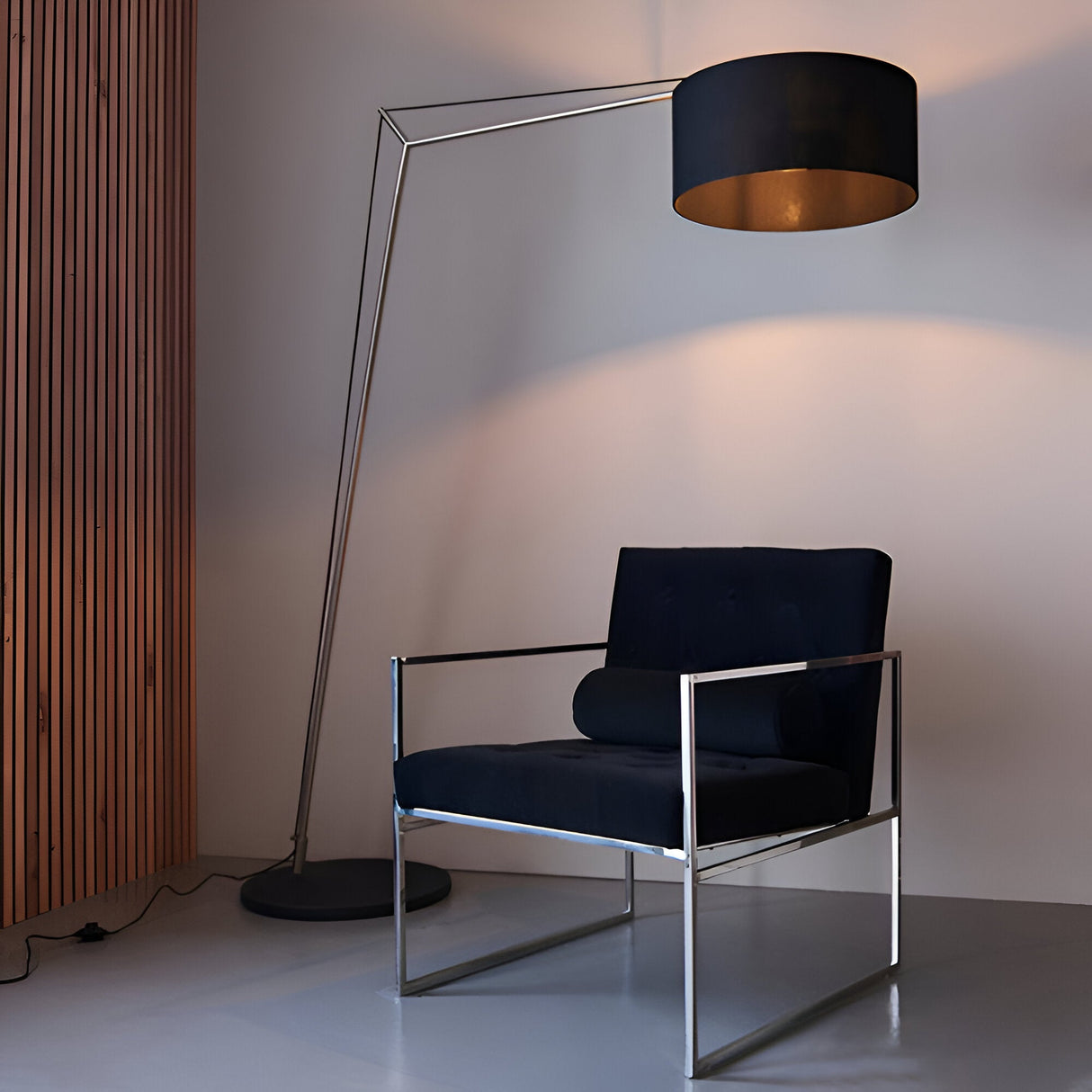 Carlfield Floor Lamp in matt nickel with a tall cantilevered arm and black fabric drum shade, shown beside a black velvet armchair in a living room.