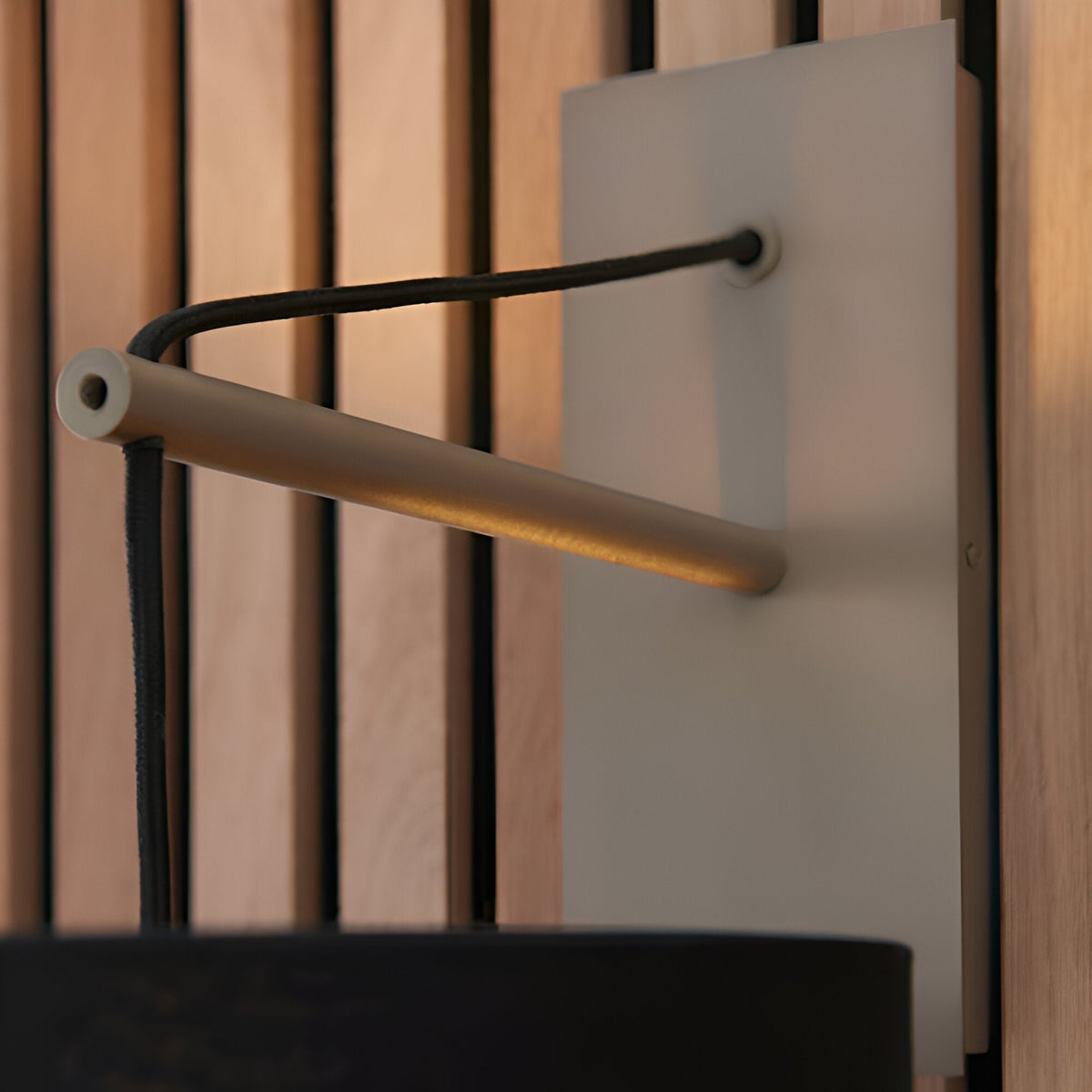 Carlfield Wall Light in Nickel, close-up of the matt nickel stem and black base with black fabric cotton shade against a wood slat background.