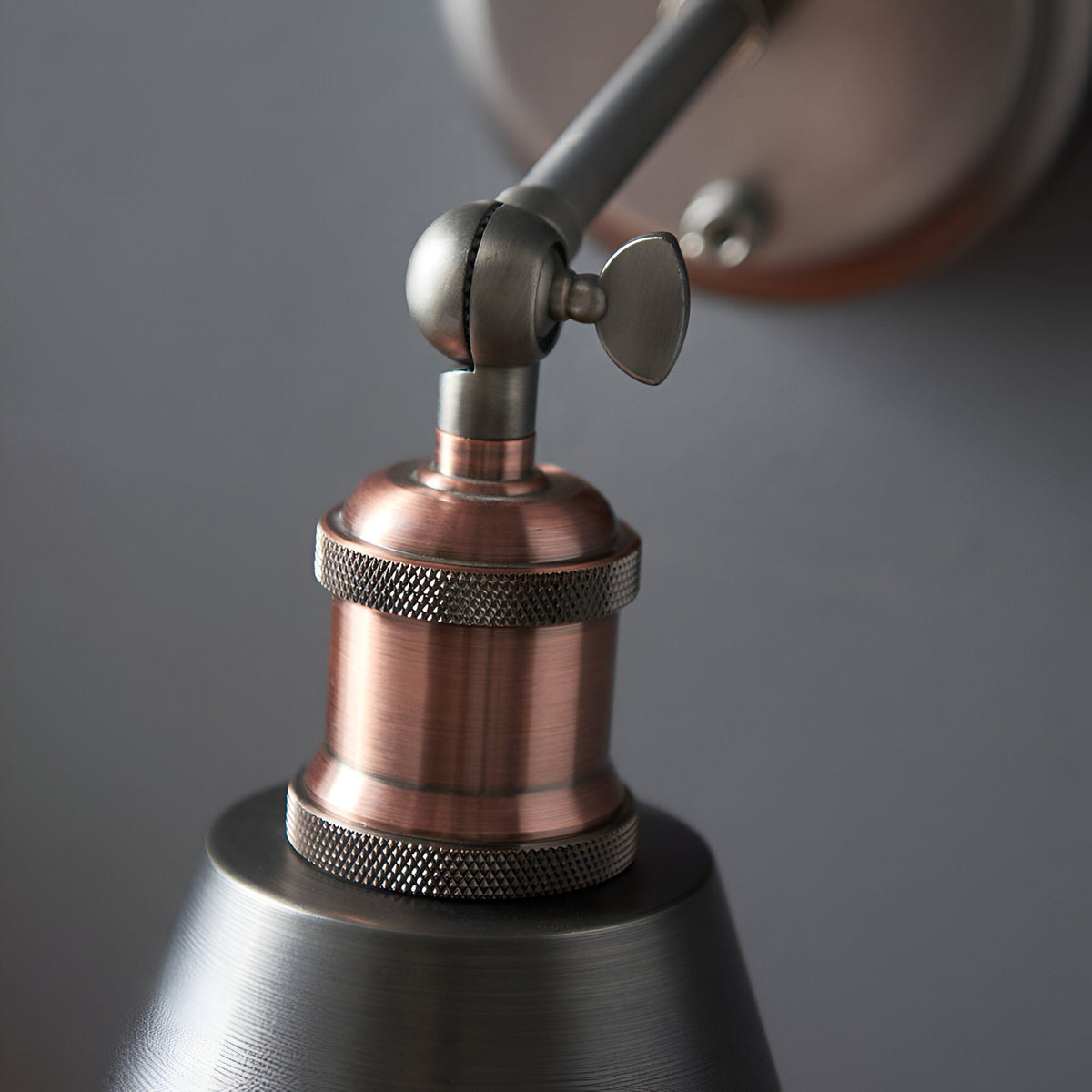 Close-up of the Endon Brackley wall light showing the aged copper lamp holder, knurled rings, adjustable pewter head joint with wing screw, and metal shade.