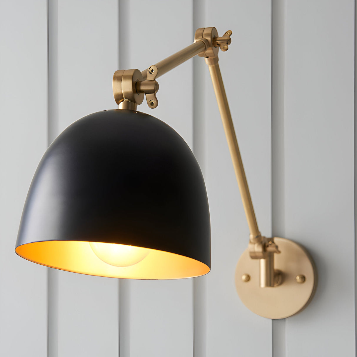 Caldhurst Wall Light in brass and black with adjustable dual-arm bracket and matt black dome shade featuring a brass interior.
