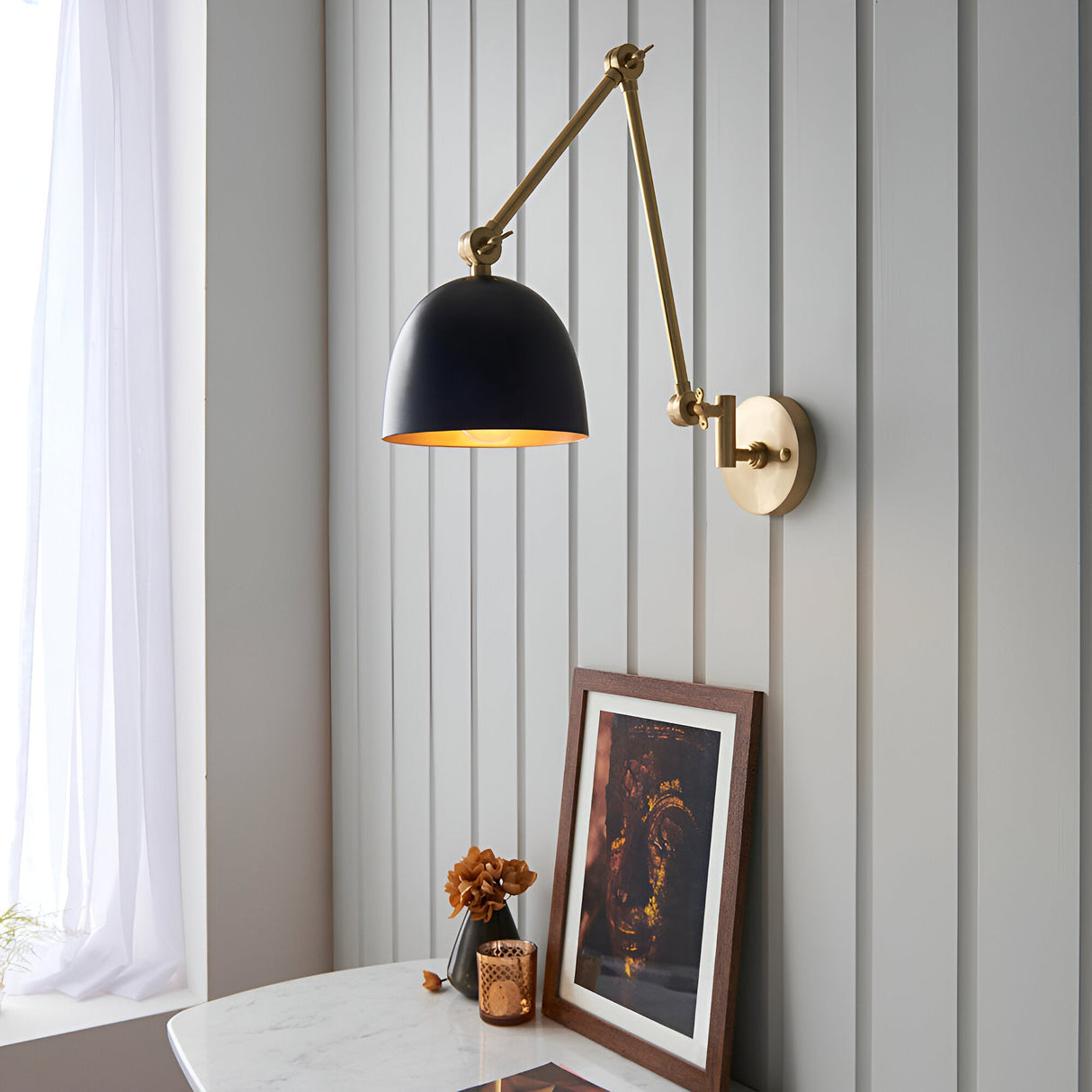 Caldhurst Wall Light in brass with a matt black shade and adjustable jointed arm, mounted on a grey panelled wall above a marble table.