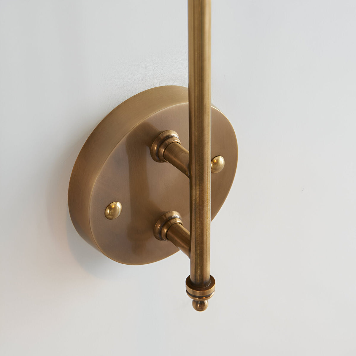 Chartmere Wall Light in antique brass, close-up of round wall plate, adjustable rod arm and decorative brass details on a white background.