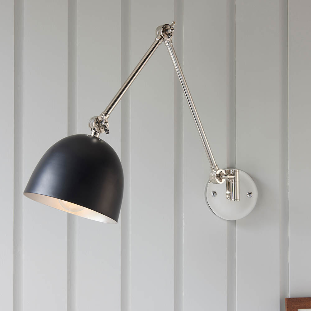 Endon Caldhurst adjustable wall light with polished nickel articulated arm and matt black dome shade, mounted on a grey panelled wall.