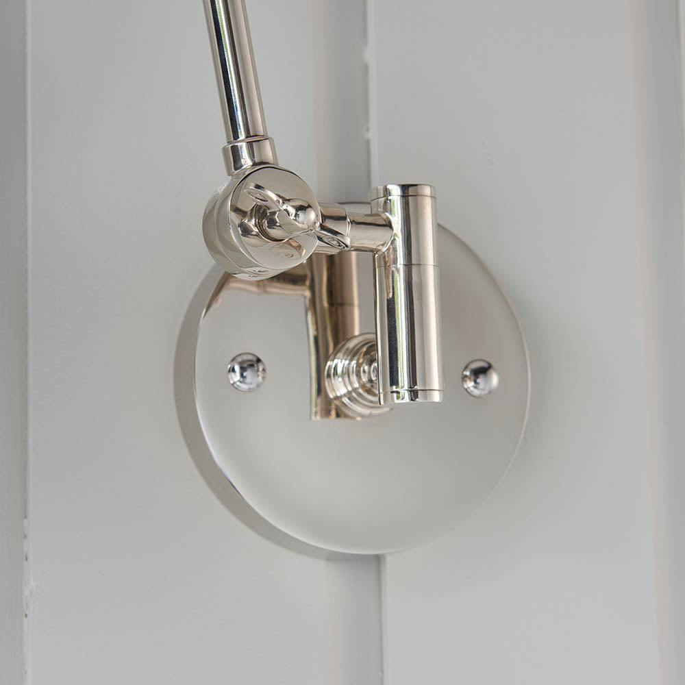 Close-up of Endon Caldhurst wall light mounting, showing polished nickel adjustable joint and round backplate with visible fixing screws against a pale wall.