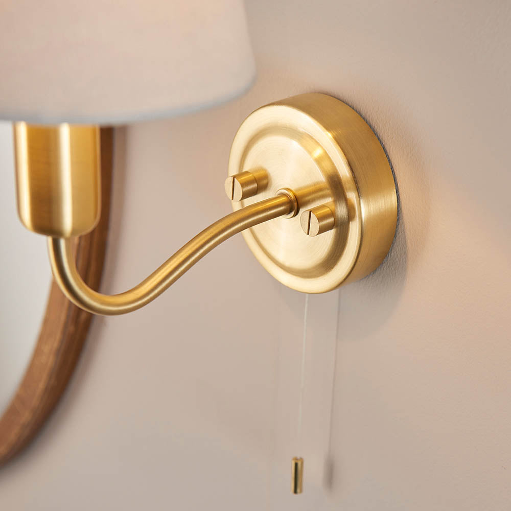Close-up of Endon Bevton bathroom wall light showing satin brass backplate, curved arm and pull cord switch mounted on a neutral wall.