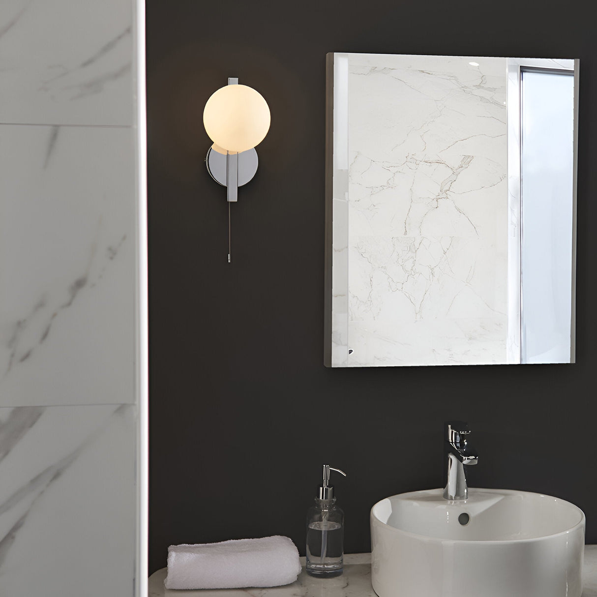 Endon Kelham bathroom wall light in chrome with opal glass sphere and pull cord, mounted on a dark wall beside a marble-framed mirror above a basin.