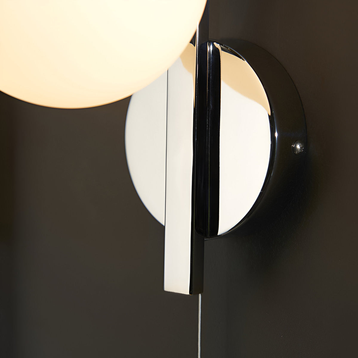 Close-up of Endon Kelham bathroom wall light in chrome, showing the circular backplate and opal glass globe mounted on a dark wall.