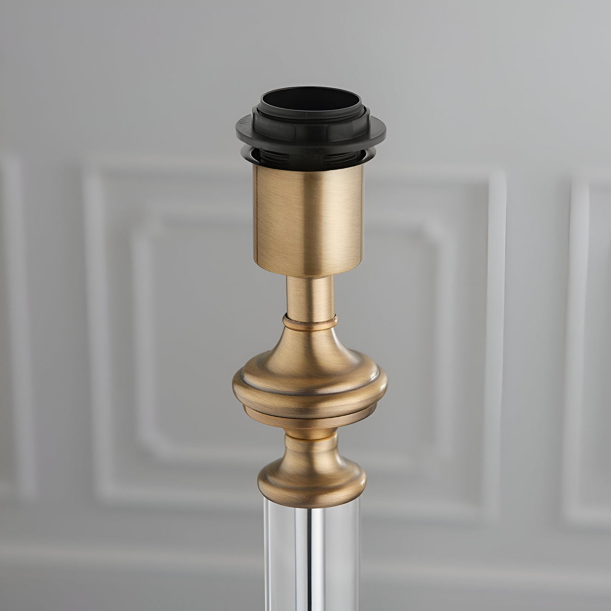 Close-up of Endon Aldmont table lamp base showing antique brass detailing, clear glass column, and E27 bulb holder against a light panelled background.