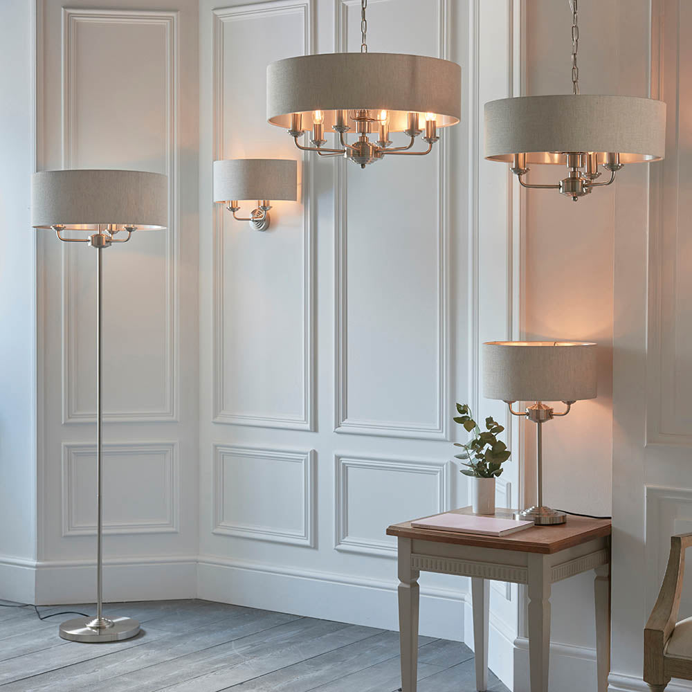 Brenley 3 Light Floor Lamp in brushed chrome with a wide linen drum shade, shown in a panelled living room alongside matching pendant and table lamps.