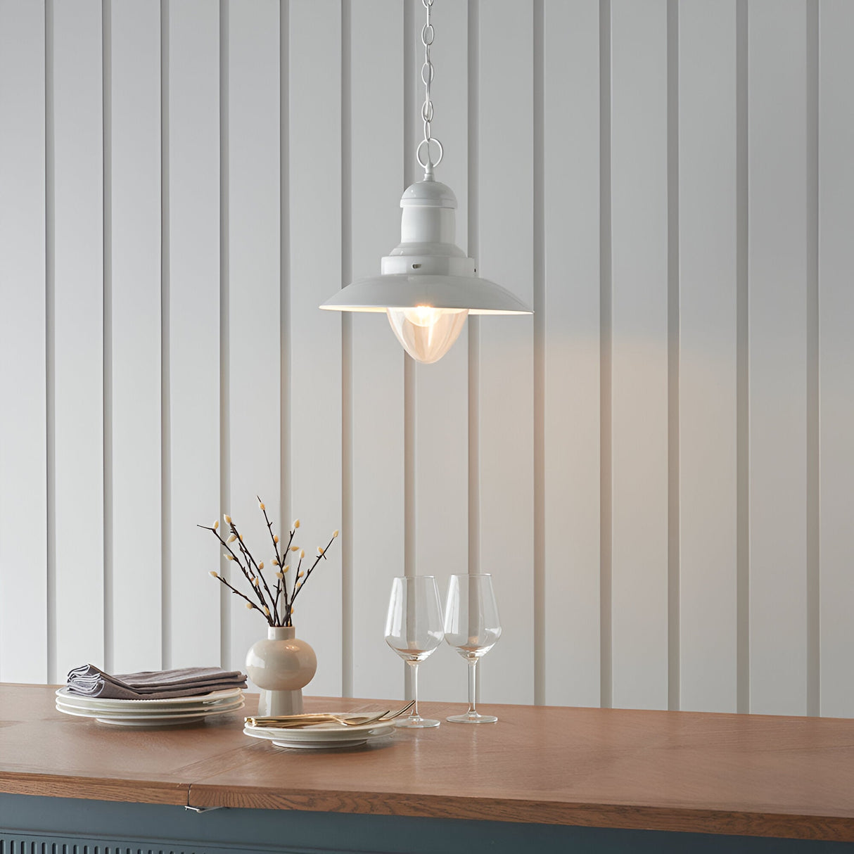 Endon Chartford cream gloss pendant light with shaped clear glass shade and chain suspension, hung above a wooden countertop against panelled walls.
