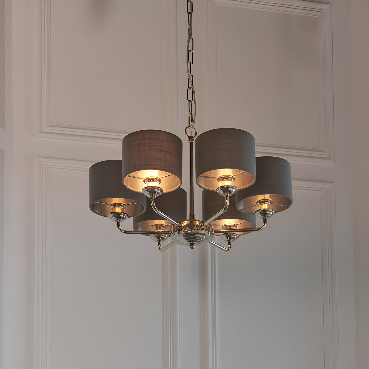 Endon Brenley V3 six-light pendant in nickel and chrome with grey linen shades and metallic inner lining, suspended on a chain against white panelled wall.