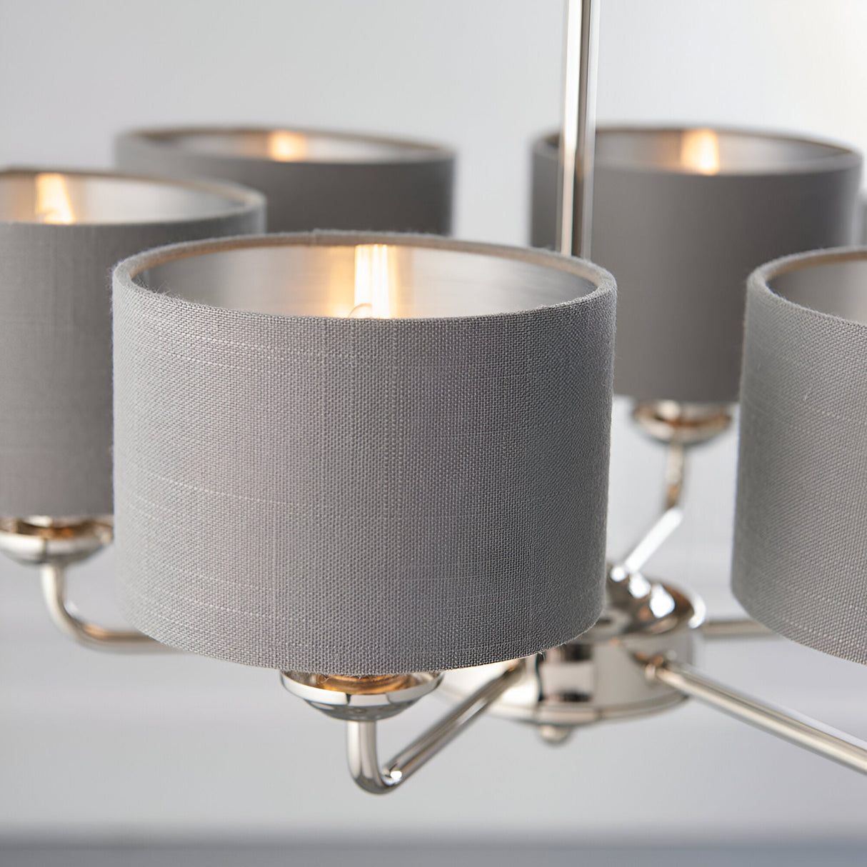 Close-up of the Endon Brenley V3 6 light pendant showing grey linen shades with brushed metallic inner linings on a polished nickel and chrome frame.