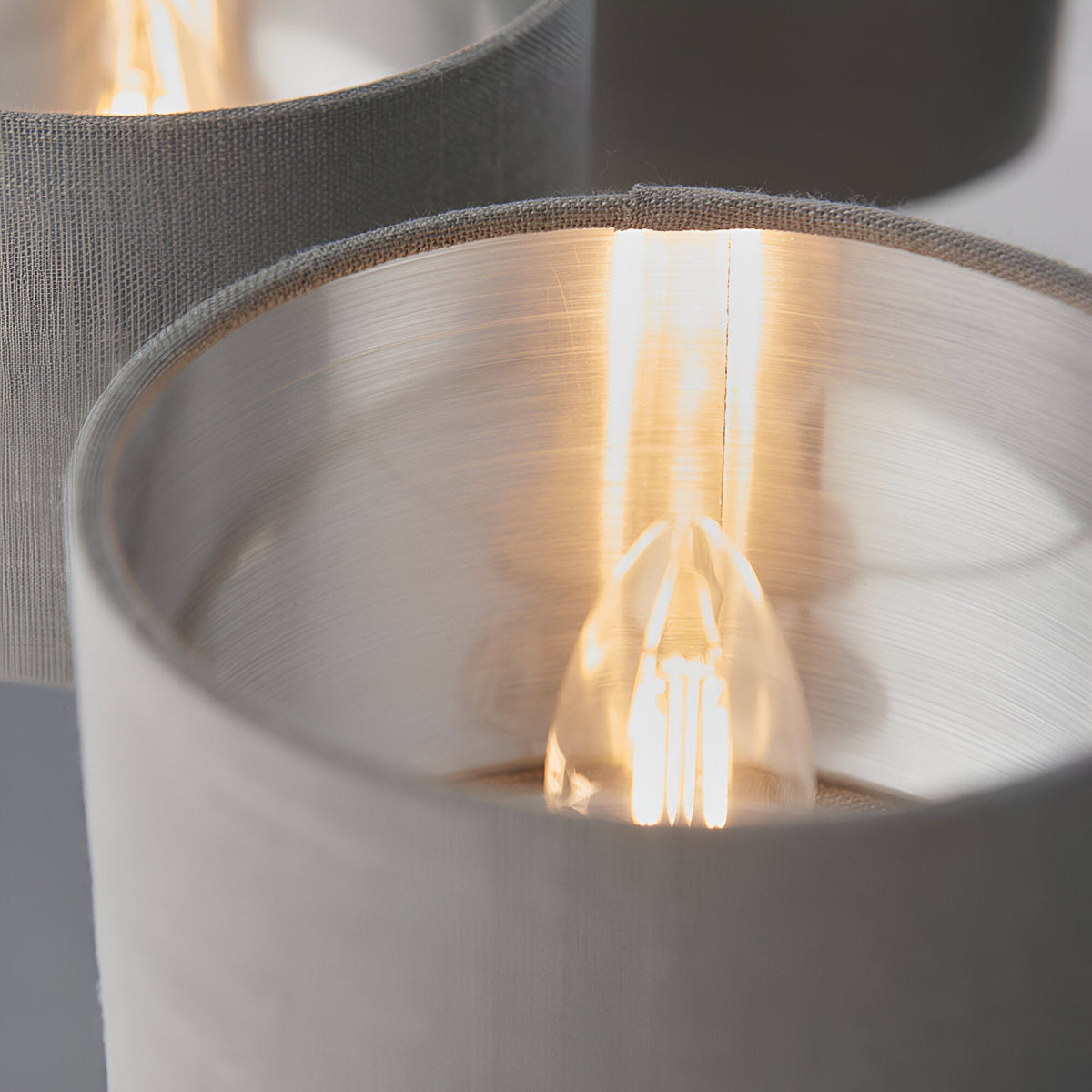 Close-up of Endon Brenley V3 6 light pendant showing grey linen shades with brushed metallic inner lining and lit E14 filament lamp.