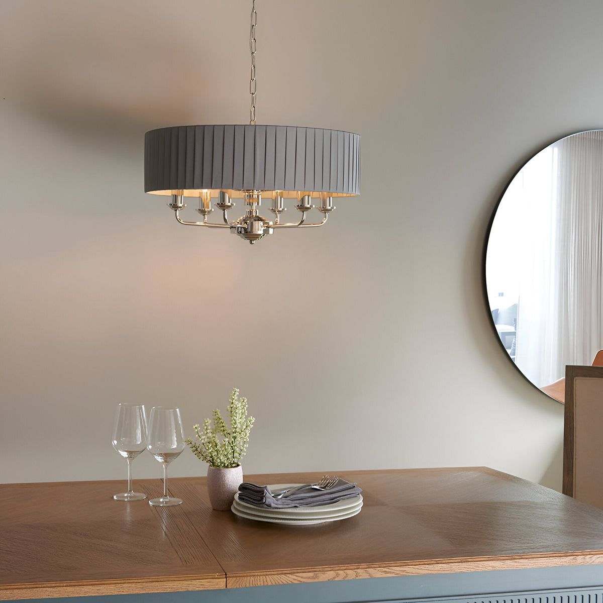 Brenley V1 6 Light Pendant in nickel and chrome with pleated grey fabric drum shade, hung above a dining table in a neutral-toned room.