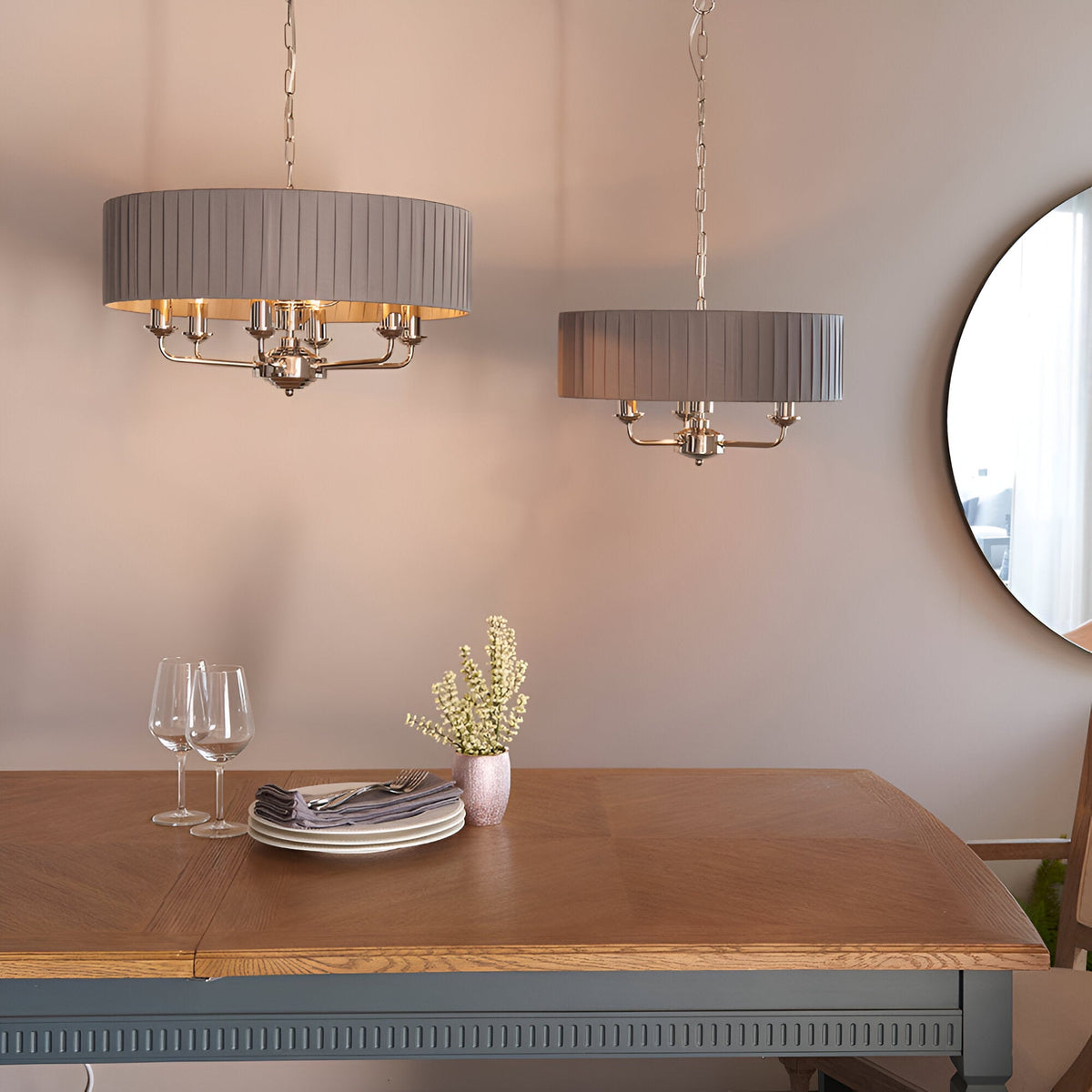 Brenley V1 6-light pendant with pleated grey fabric drum shade and nickel arms, shown above a wood dining table with a second matching pendant nearby.