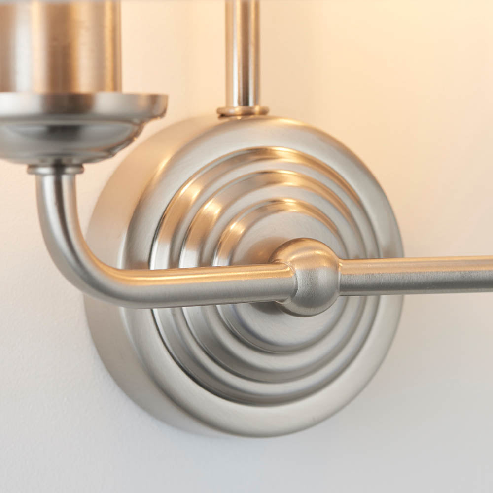 Close-up of the Brenley 2 Light Wall Light's chrome backplate with ribbed detailing and brass arm, showing the joint where the metal fittings connect.