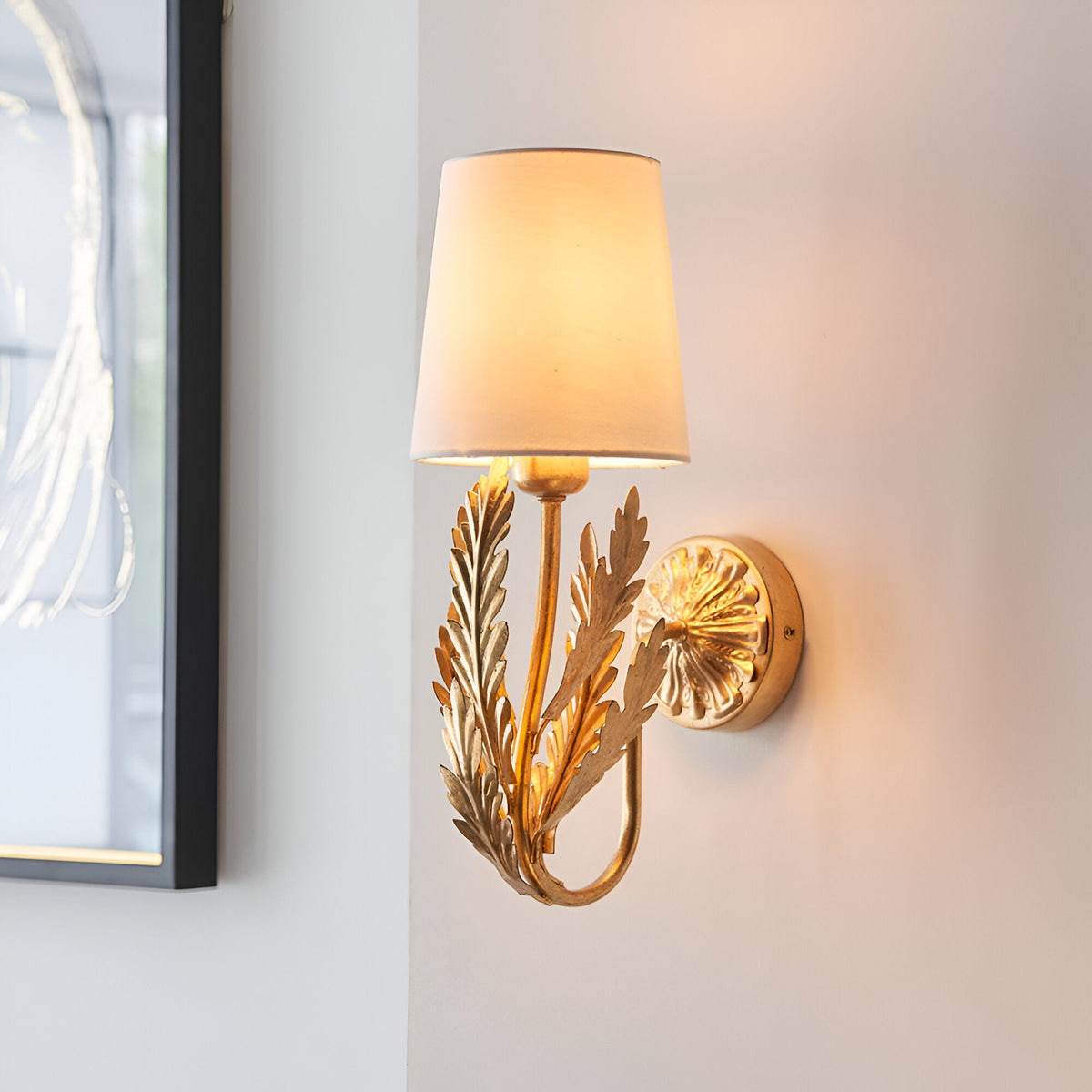 Colette Wall Light in gold and cream, featuring layered leaf detailing and a cream fabric shade, mounted on a light wall beside a mirror.