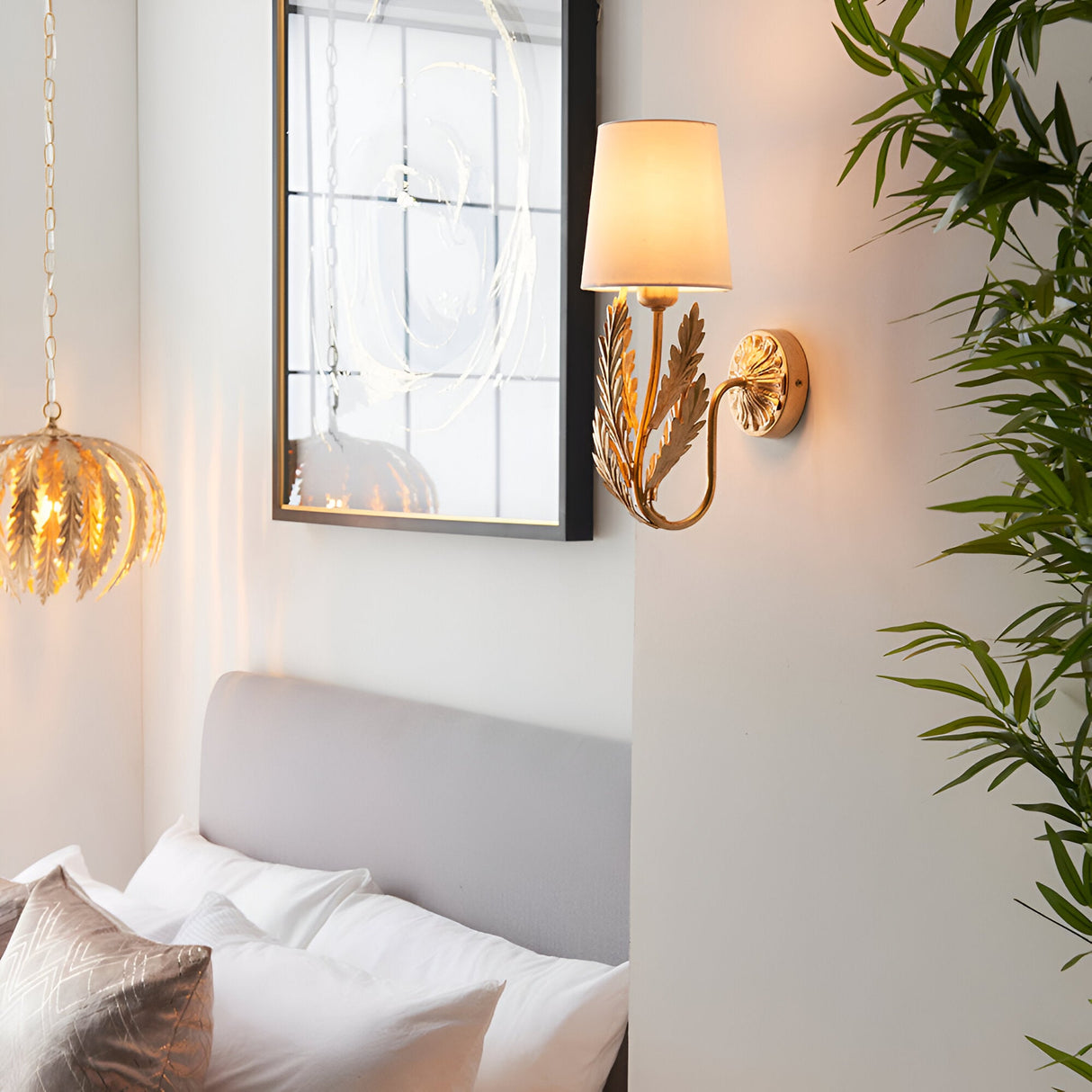 Colette Wall Light in gold with layered leaf detail and cream fabric shade, mounted above a bed in a bedroom setting.