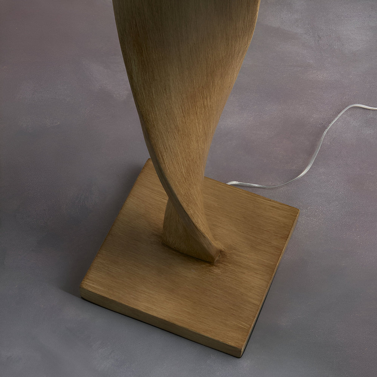 Endon Alcott floor lamp base detail showing the spiralling light oak effect wood column set on a square plinth, with black cable trailing across grey flooring.