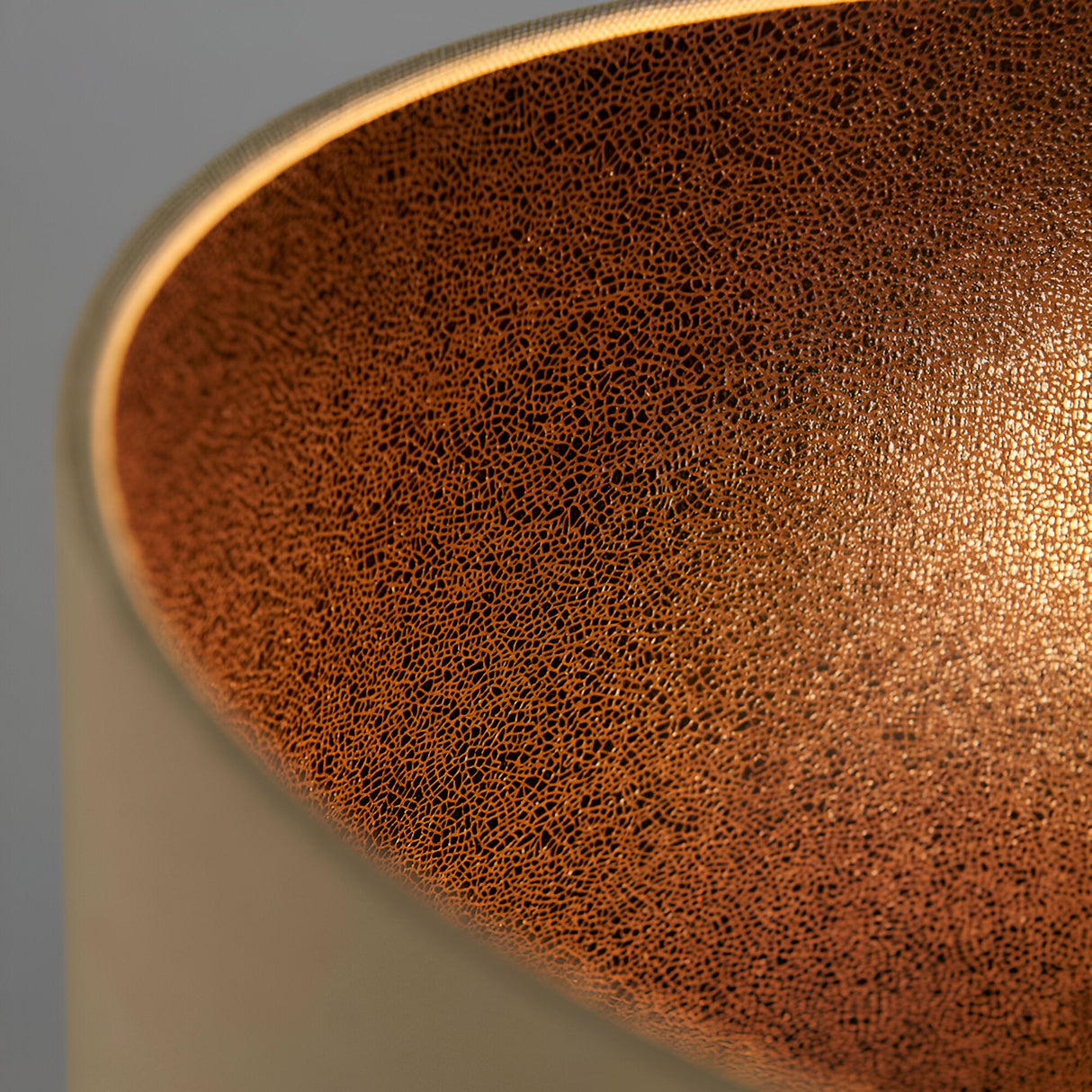 Close-up of the Alcott Table Lamp's natural linen shade interior, showing crackled bronze-tone texture illuminated from within, set on a light oak-effect base.