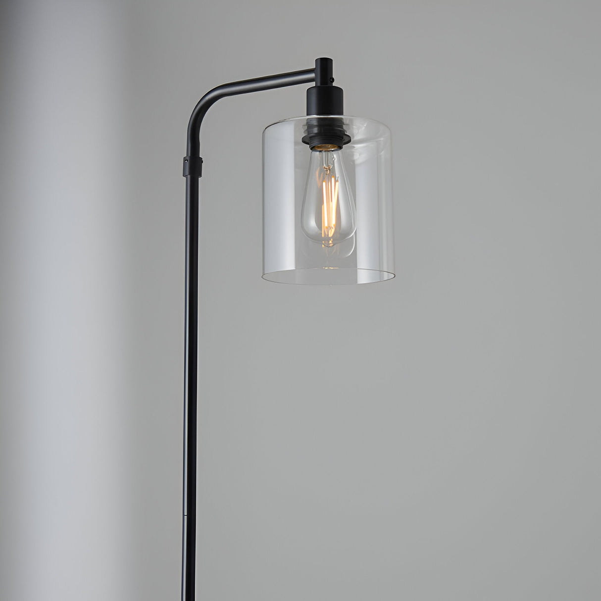 Cranmere Floor Lamp in matt black metal with a clear glass shade and exposed filament bulb, angled top detail against a plain grey background.
