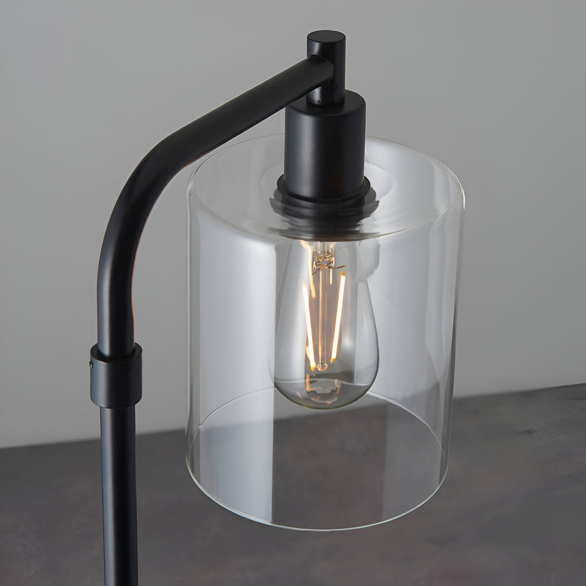Cranmere Floor Lamp in matt black metal, close-up of the clear glass cylinder shade and E27 filament bulb, set against a plain grey background.