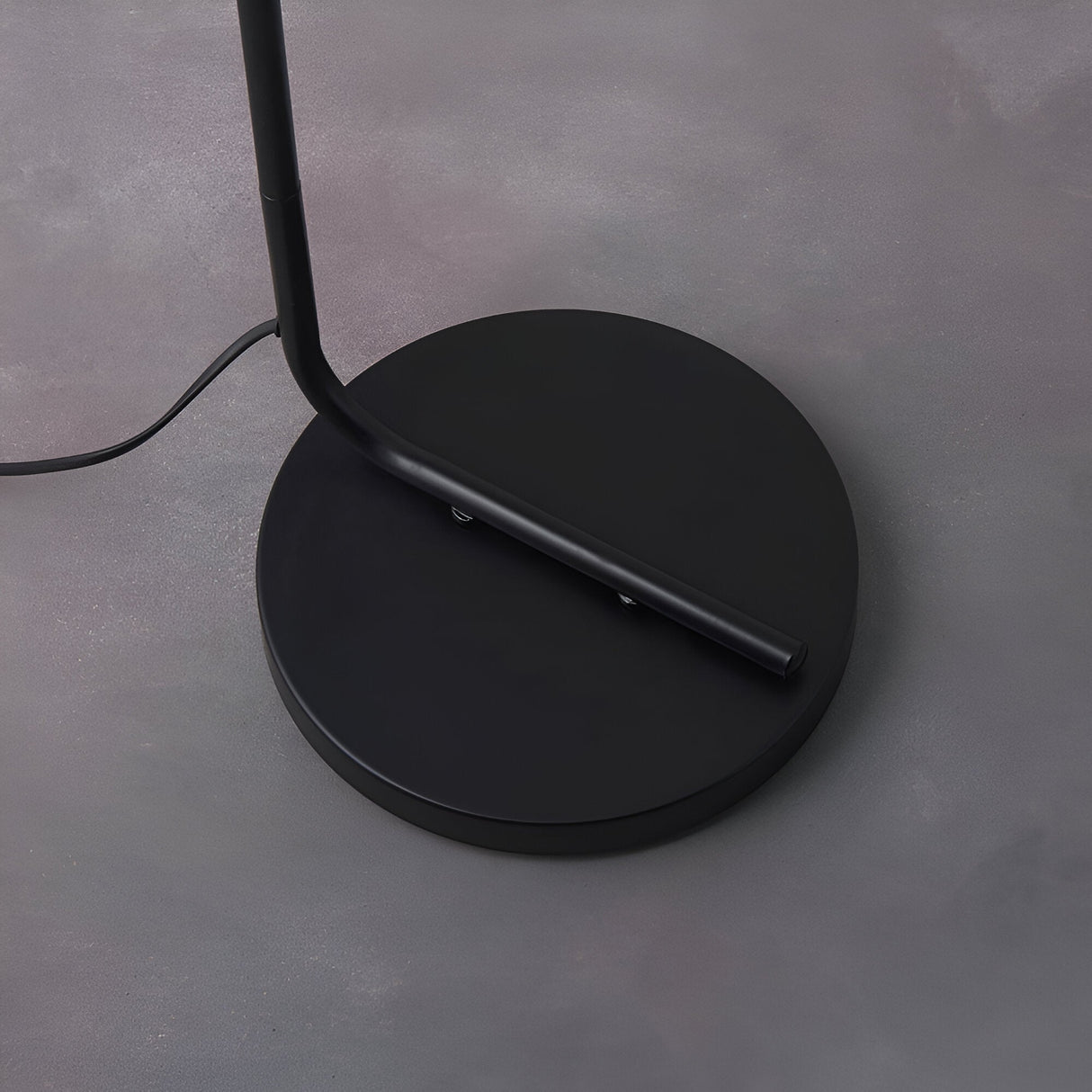 Cranmere Floor Lamp in matt black metal, close-up of angled pole and round base on a grey studio background.