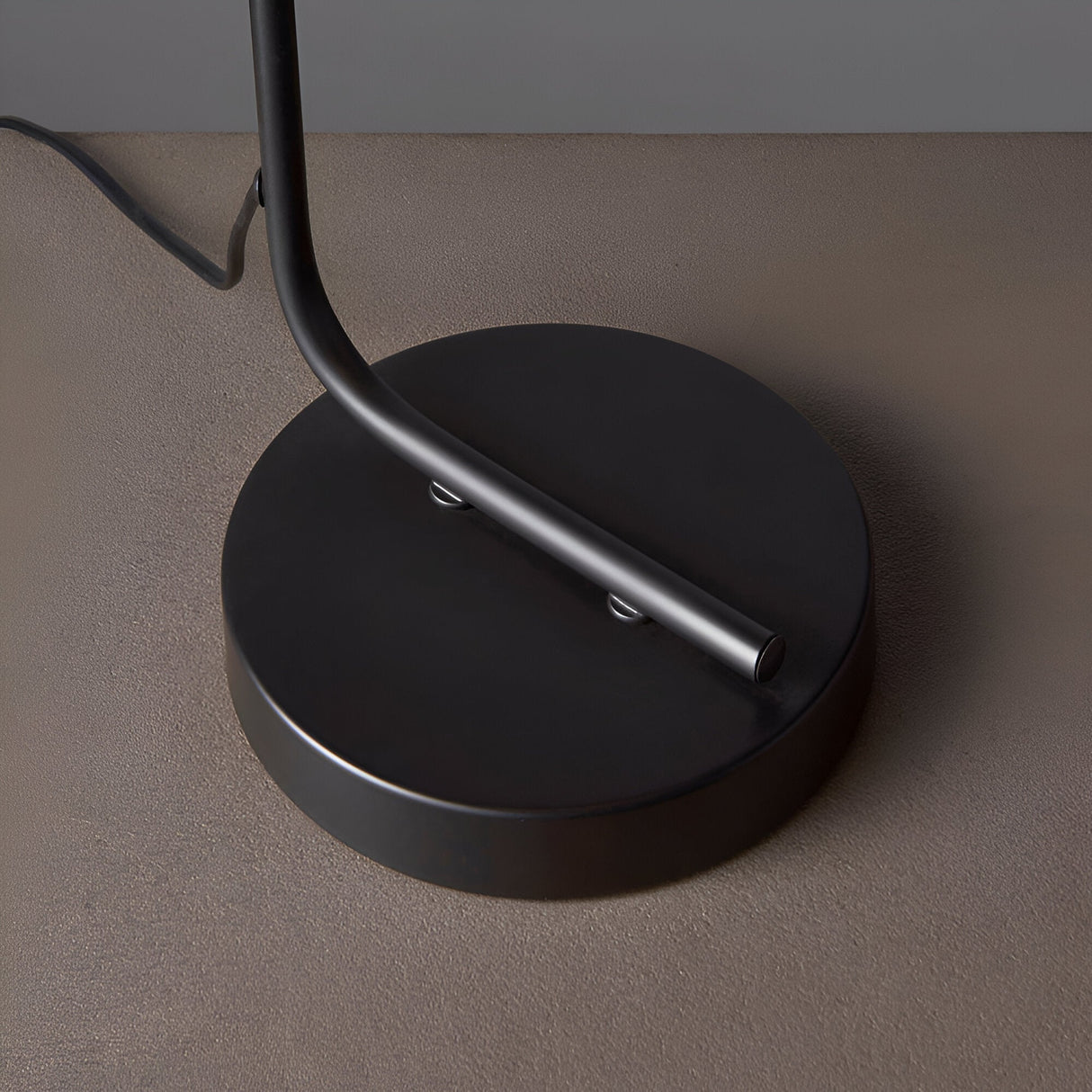 Close-up of the Endon Cranmere table lamp base, a round matt black metal disc with the curved stem rising from it and an inline switch on the flex.
