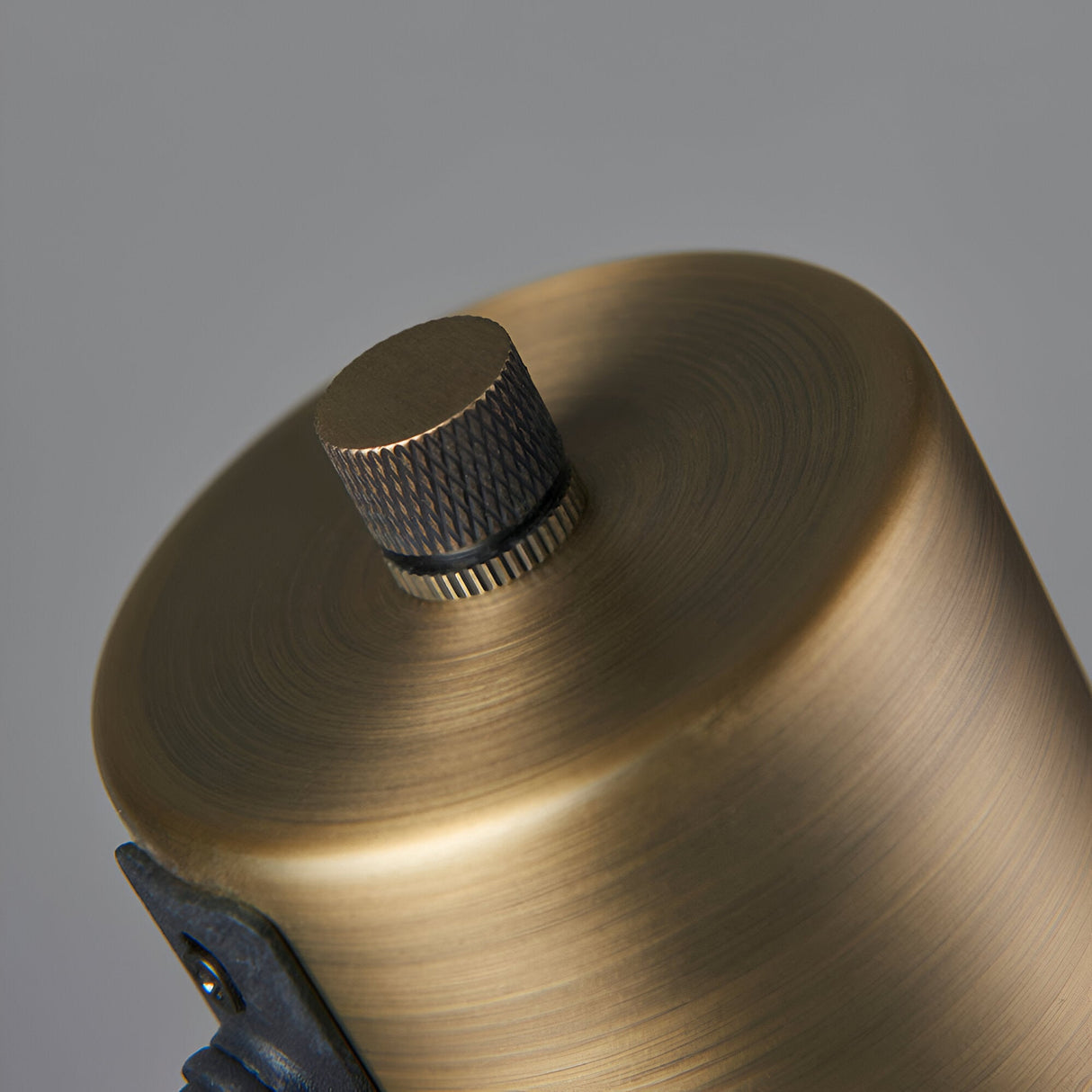 Close-up of the Carlbourne Table Lamp's cylindrical top in matt antique brass with a knurled black rotary switch, shown against a plain grey background.
