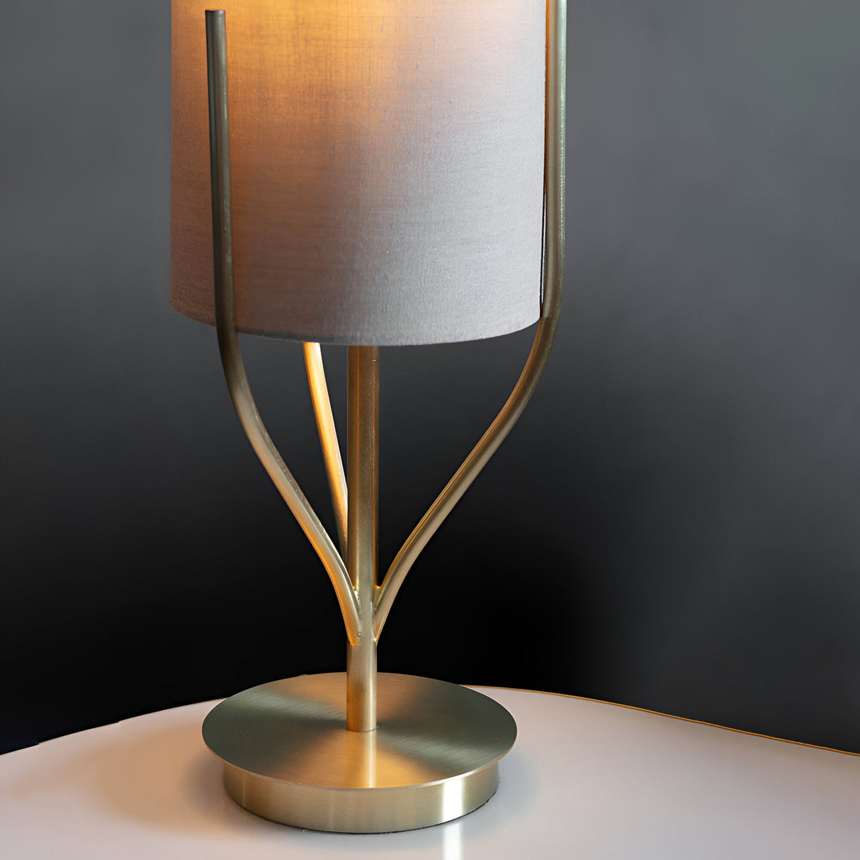 Endon Bramdon table lamp close-up showing satin brass branching stem, round base and natural linen cylinder shade on a pale surface against grey.
