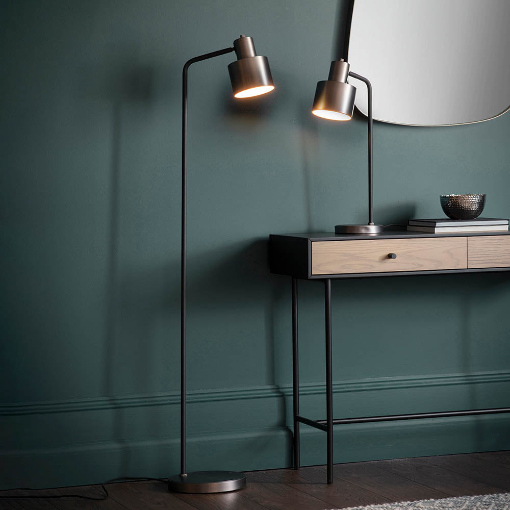 Endon Carlbourne floor lamp in brushed silver and matt black, lit beside a wooden console with matching table lamp against a dark teal wall.