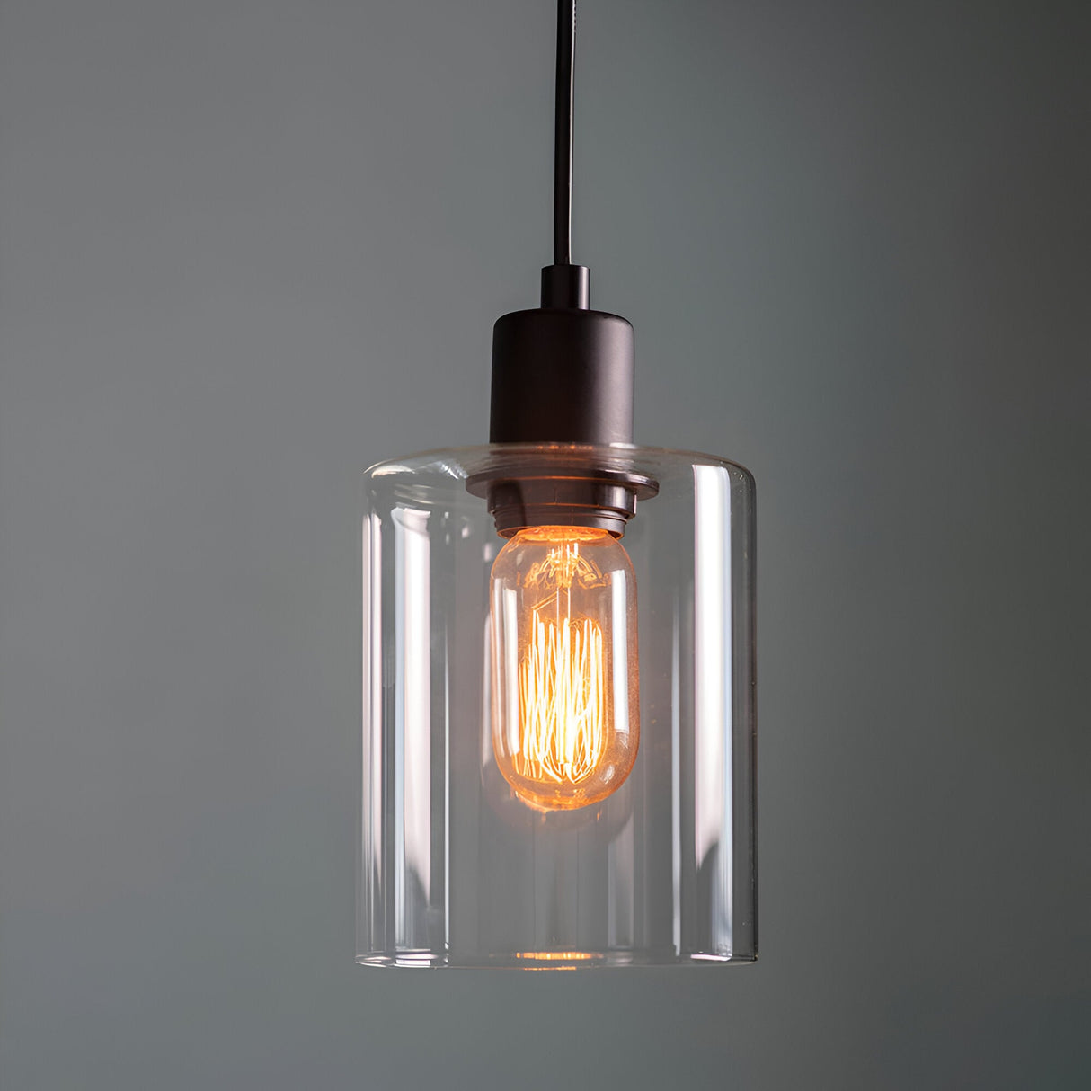 Endon Cranmere pendant light in matt black with a compact clear glass cylinder shade and exposed filament E27 bulb, shown against a grey background.