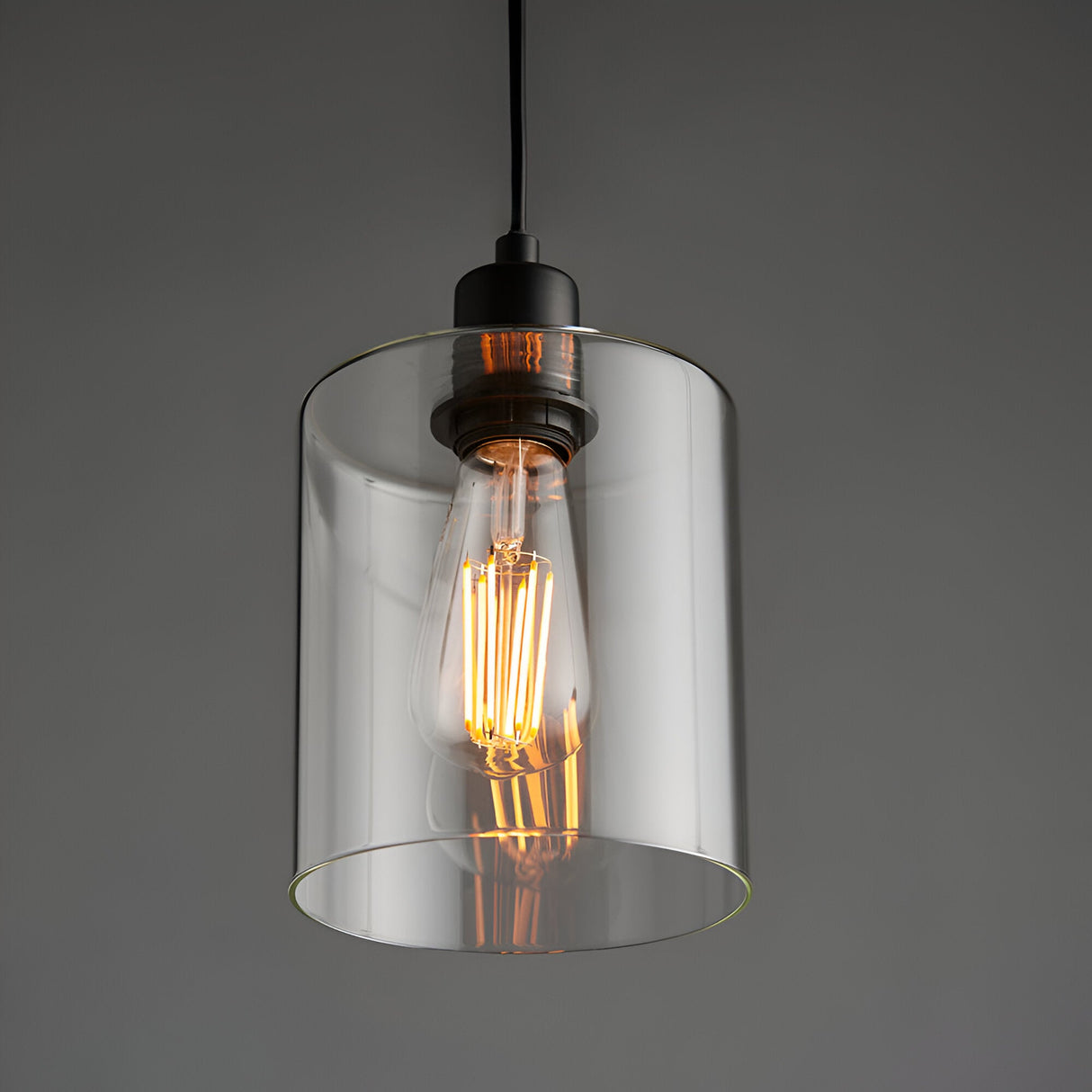 Endon Cranmere pendant light in matt black with a clear cylindrical glass shade and exposed filament E27 bulb, suspended against a grey background.
