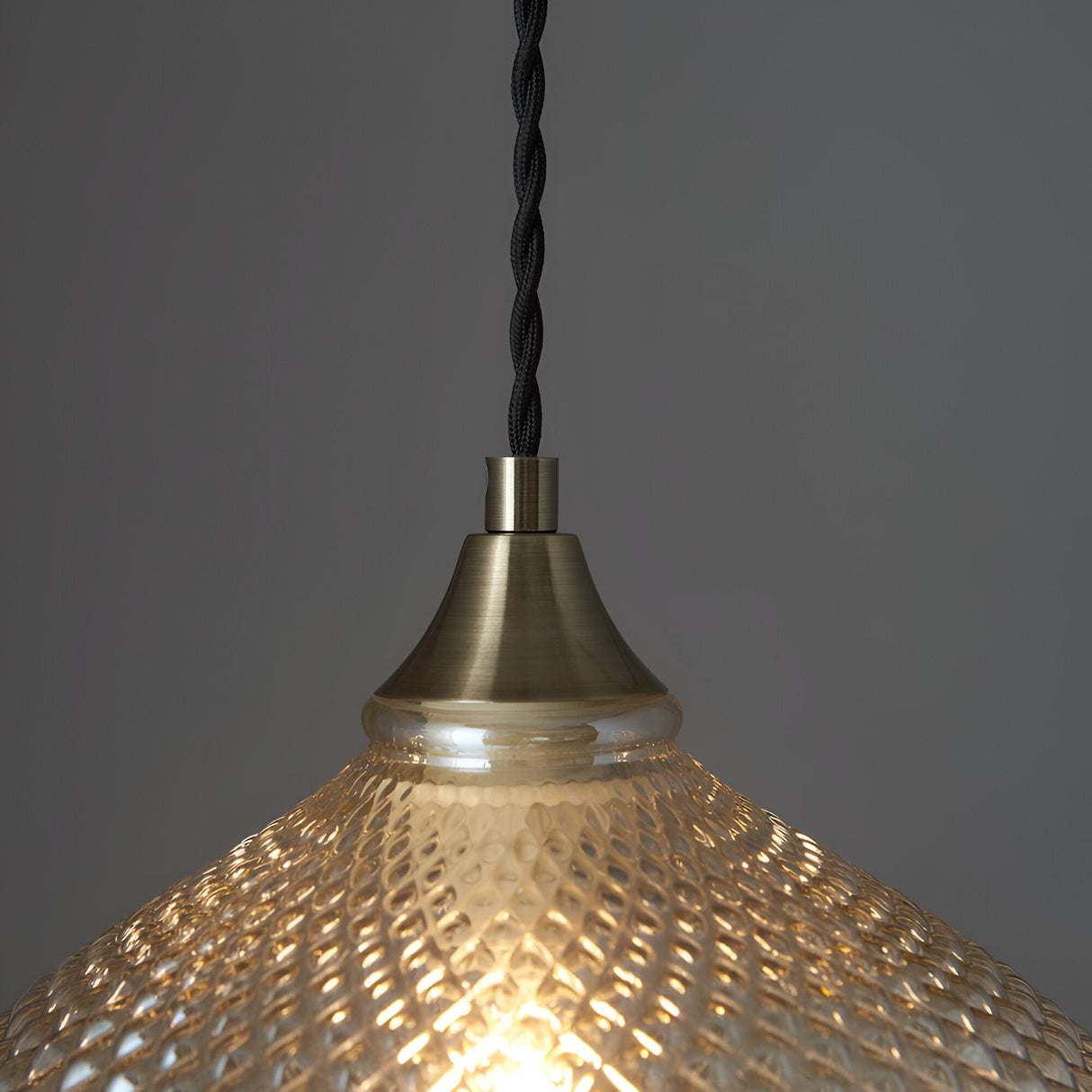 Close-up of the Endon Caldstead pendant light showing the antique brass cap and textured champagne glass shade on a black twisted fabric flex.