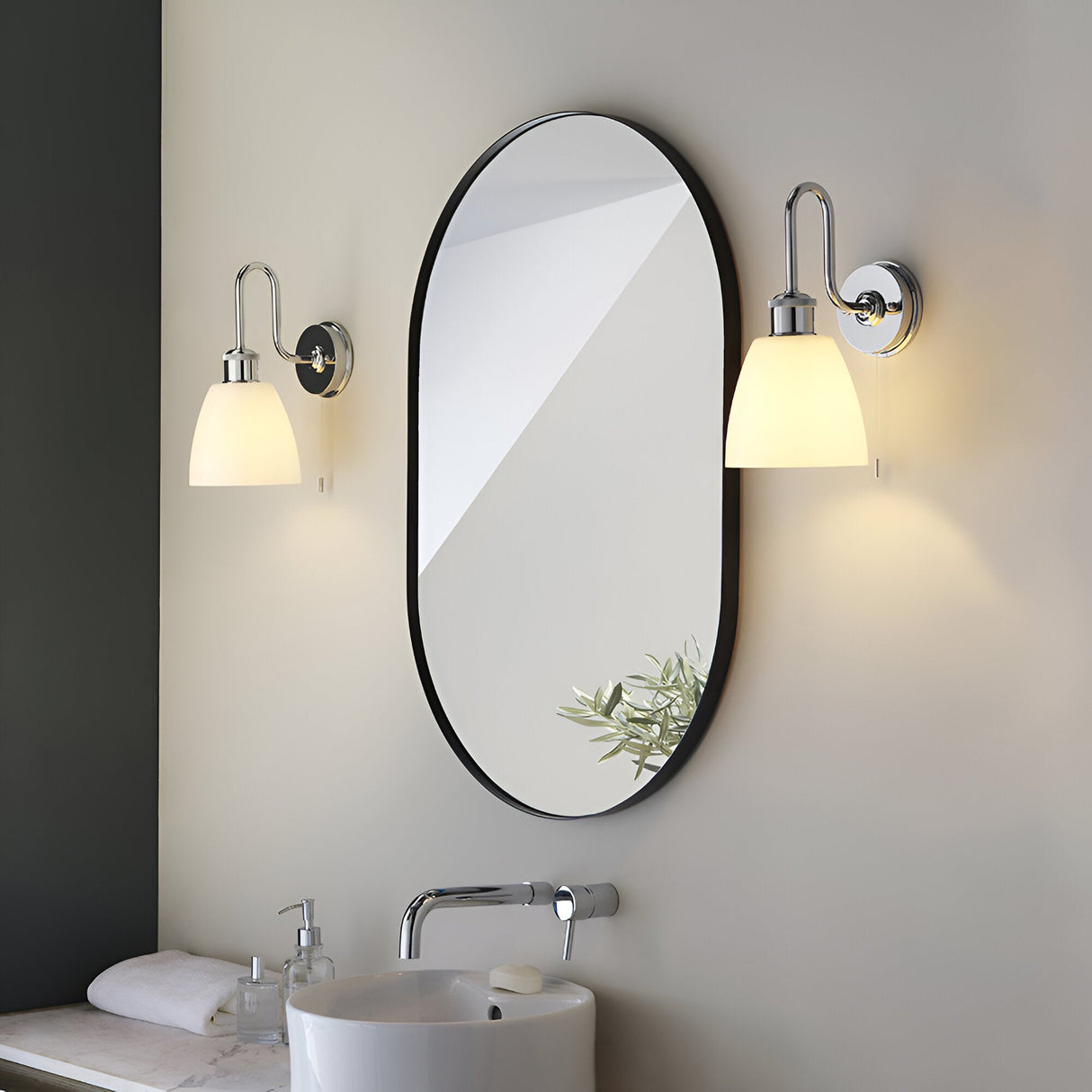 Chartdon bathroom wall lights in polished chrome with swan-neck arms and opal glass shades, mounted either side of an oval mirror above a sink.