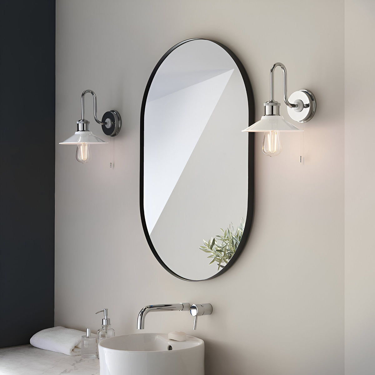 Cardew swan-neck bathroom wall lights in polished chrome with white coolie shades and pull switches, mounted either side of an oval mirror above a basin.